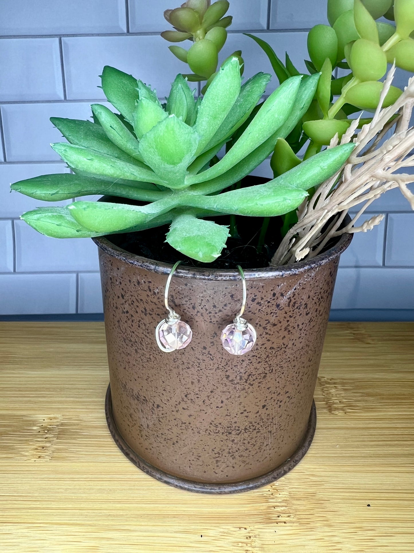 A potted succulent plant with green leaves and a hanging earring in a brown vase.
