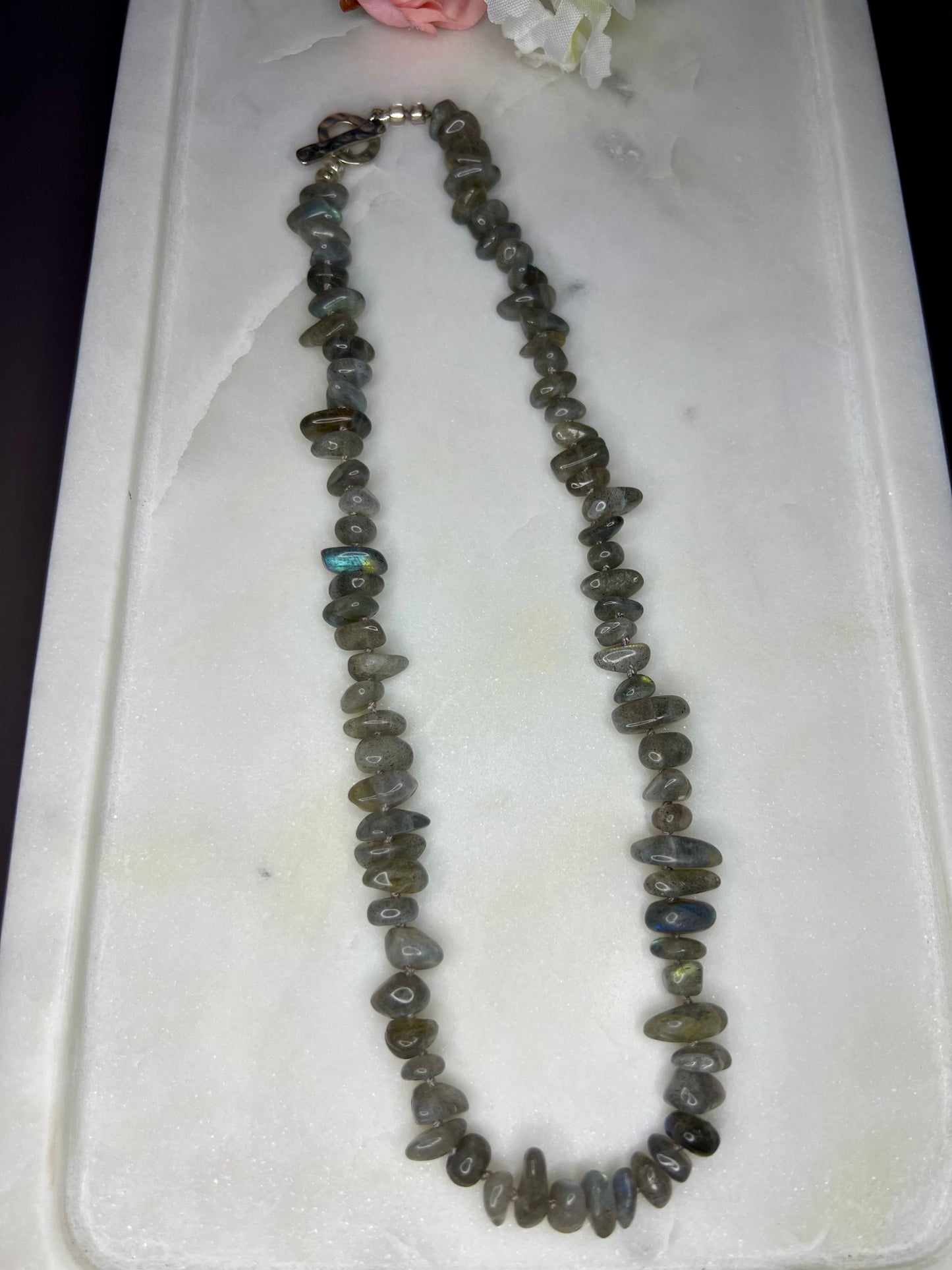 A necklace made of small, irregularly shaped stones in various shades of gray, brown, and black, resting on a white surface.