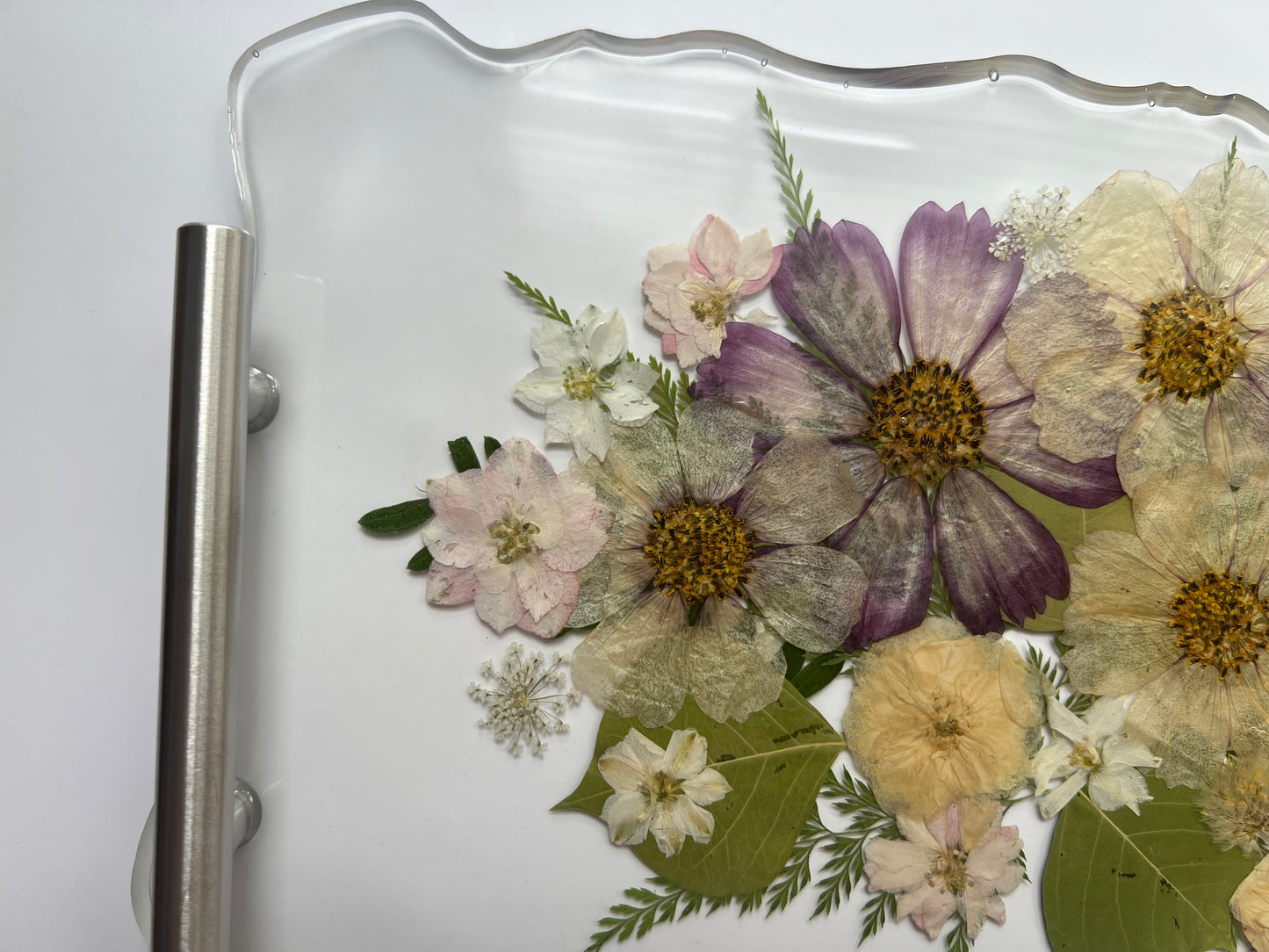 a close-up view of a glass tray with a floral arrangement of various flowers, including white, purple, and yellow flowers, along with green leaves.