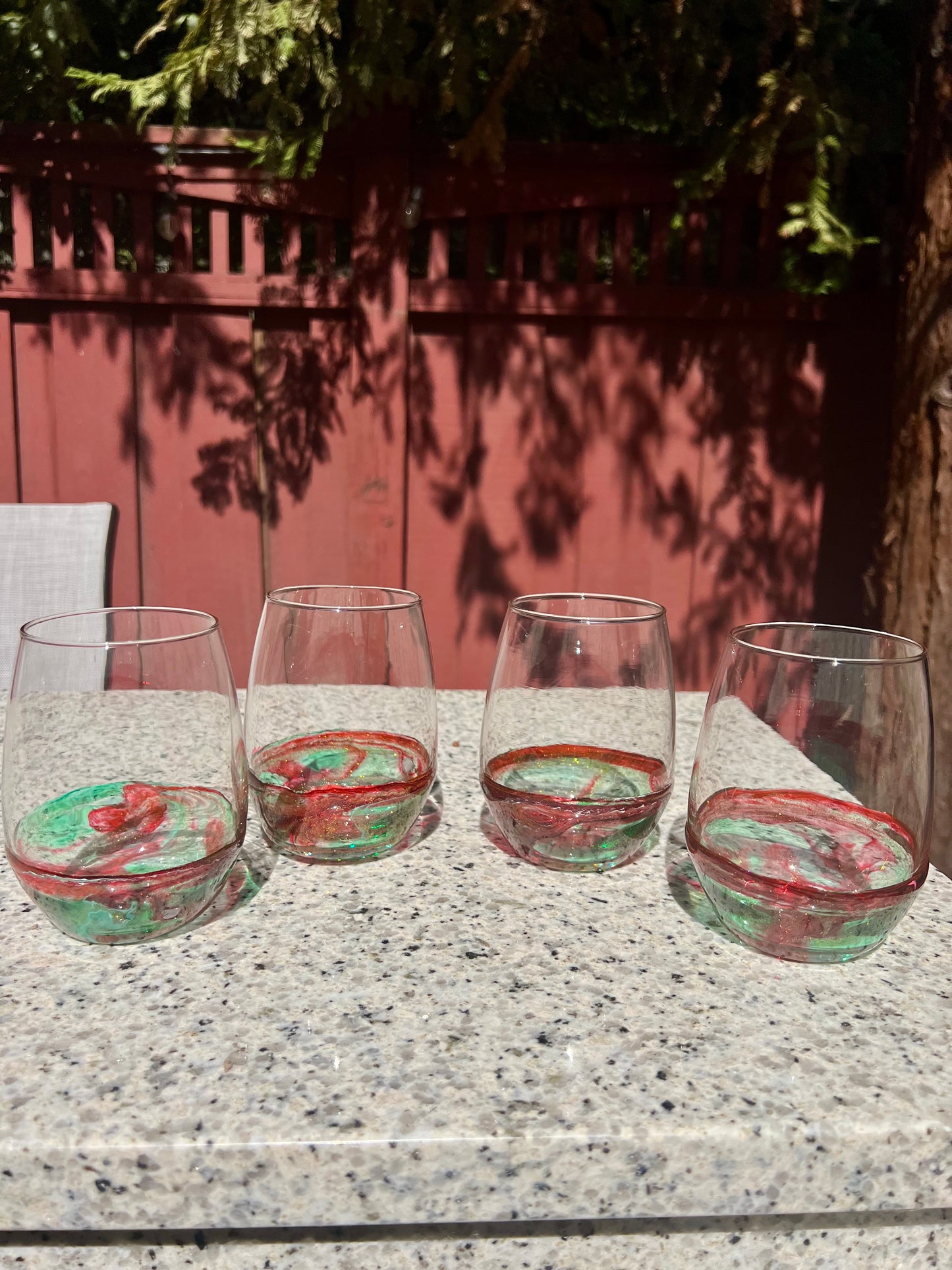 Four wine glasses with red and green swirls on the inside are arranged on a granite countertop.