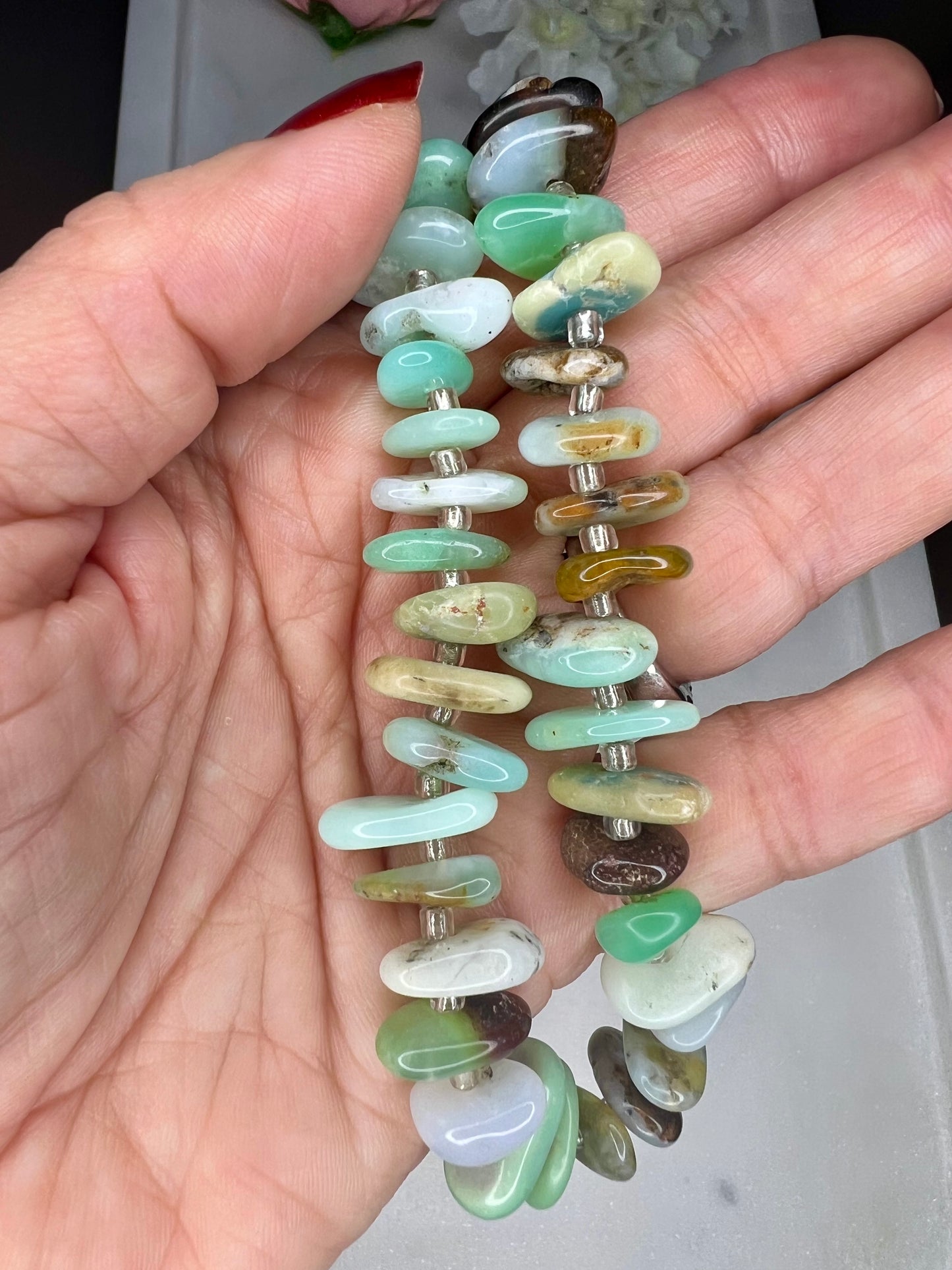 A hand is holding a necklace made of multicolored beads, including various shades of green, blue, and brown.