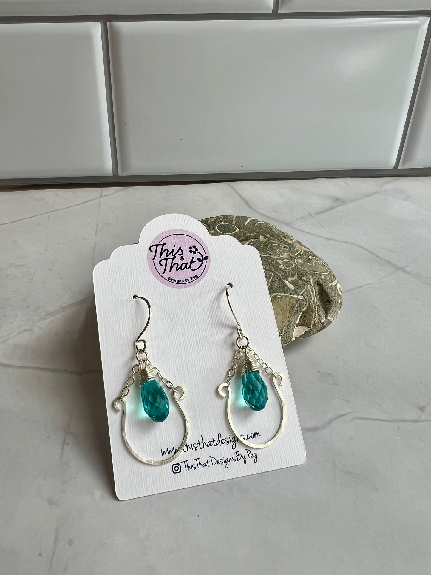 This image shows a pair of earrings with turquoise stones, displayed on a white card with a website address and a social media handle.