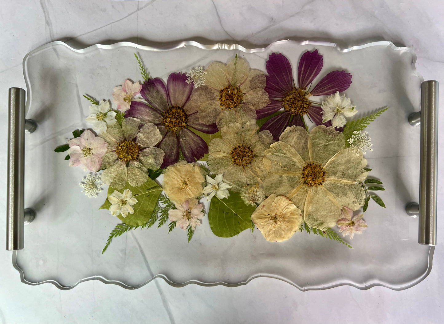 A clear glass tray with a floral arrangement of various colorful flowers, including white, purple, and yellow blooms, along with green leaves.