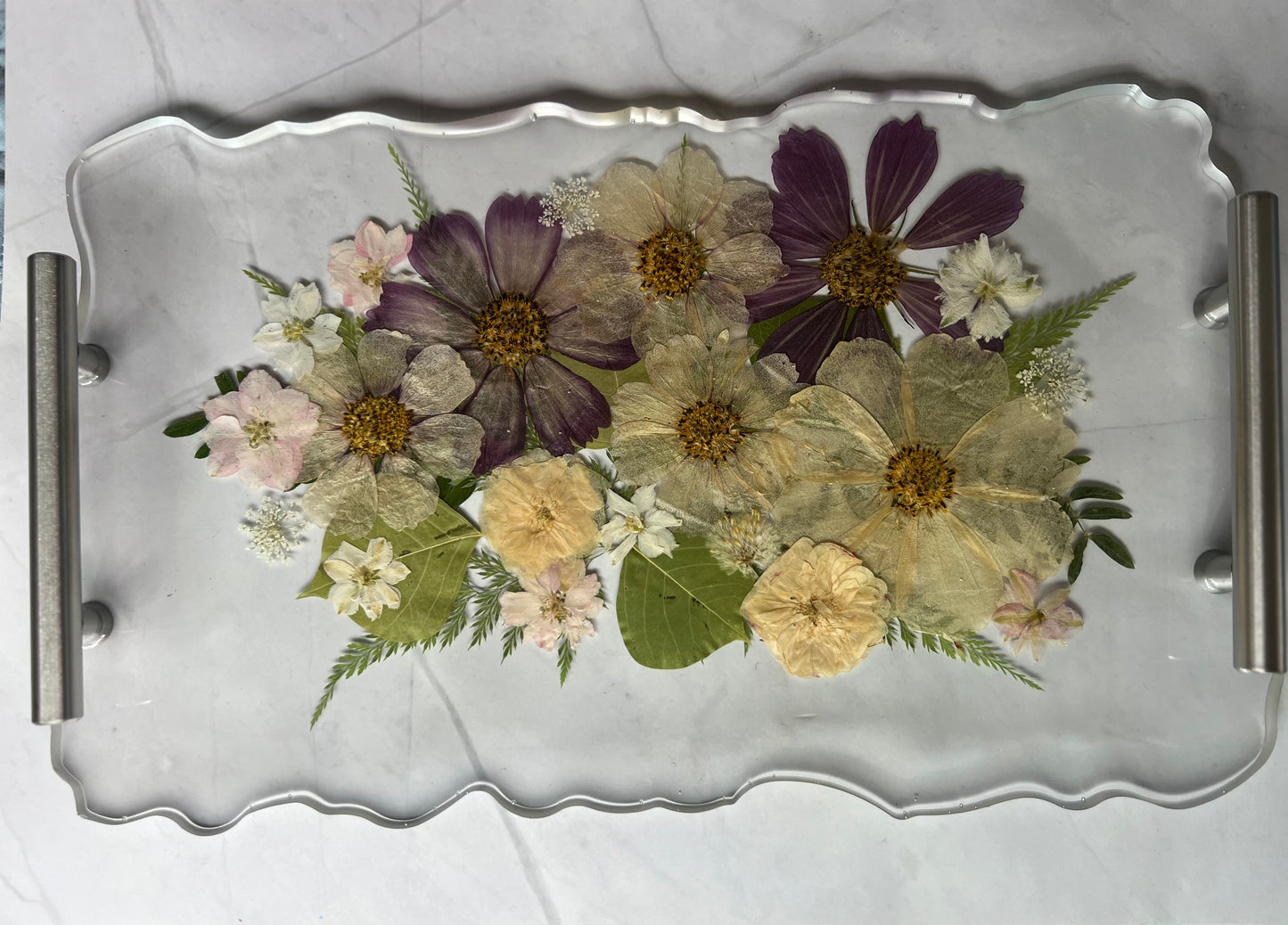 A clear glass tray with a variety of colorful flowers and leaves arranged on it.