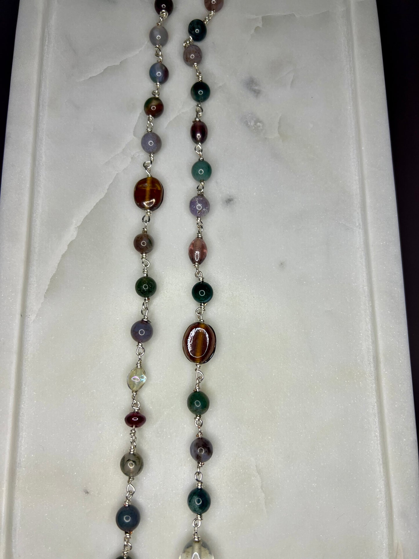 a necklace with a variety of colorful beads, including green, purple, and brown beads, arranged in a row on a white surface.