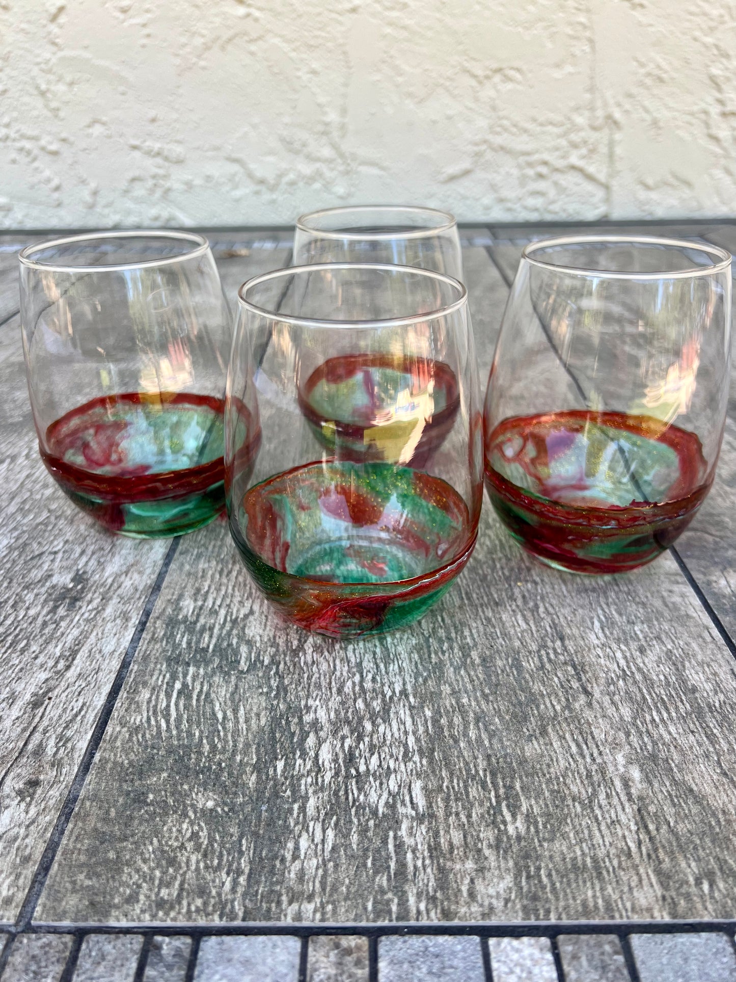 a set of four wine glasses with colorful, swirling patterns in red, green, and white colors, placed on a wooden surface.