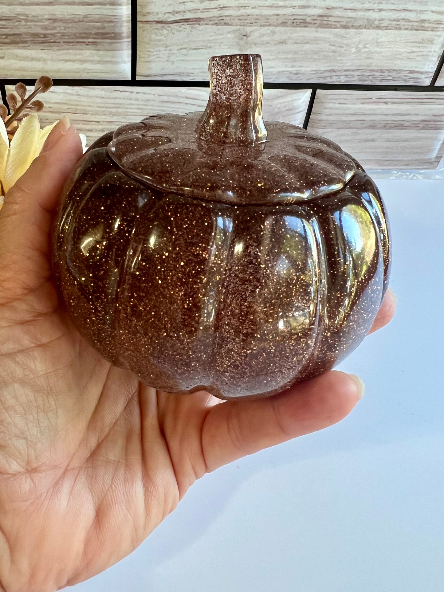 A hand holding a brown glittery pumpkin-shaped container with a lid.