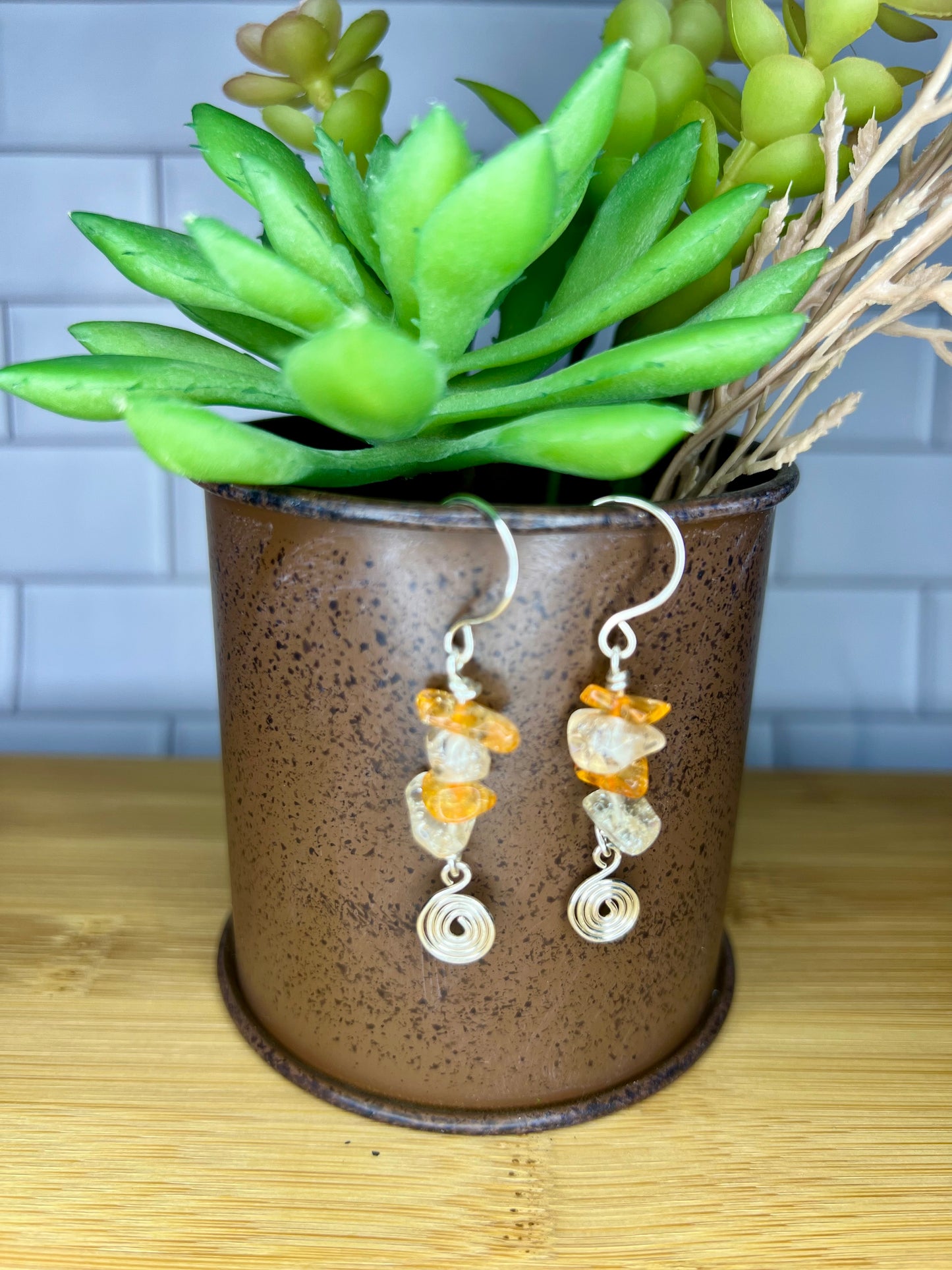 A pair of earrings with orange and white stones hanging from them, placed in a brown ceramic container or vase.