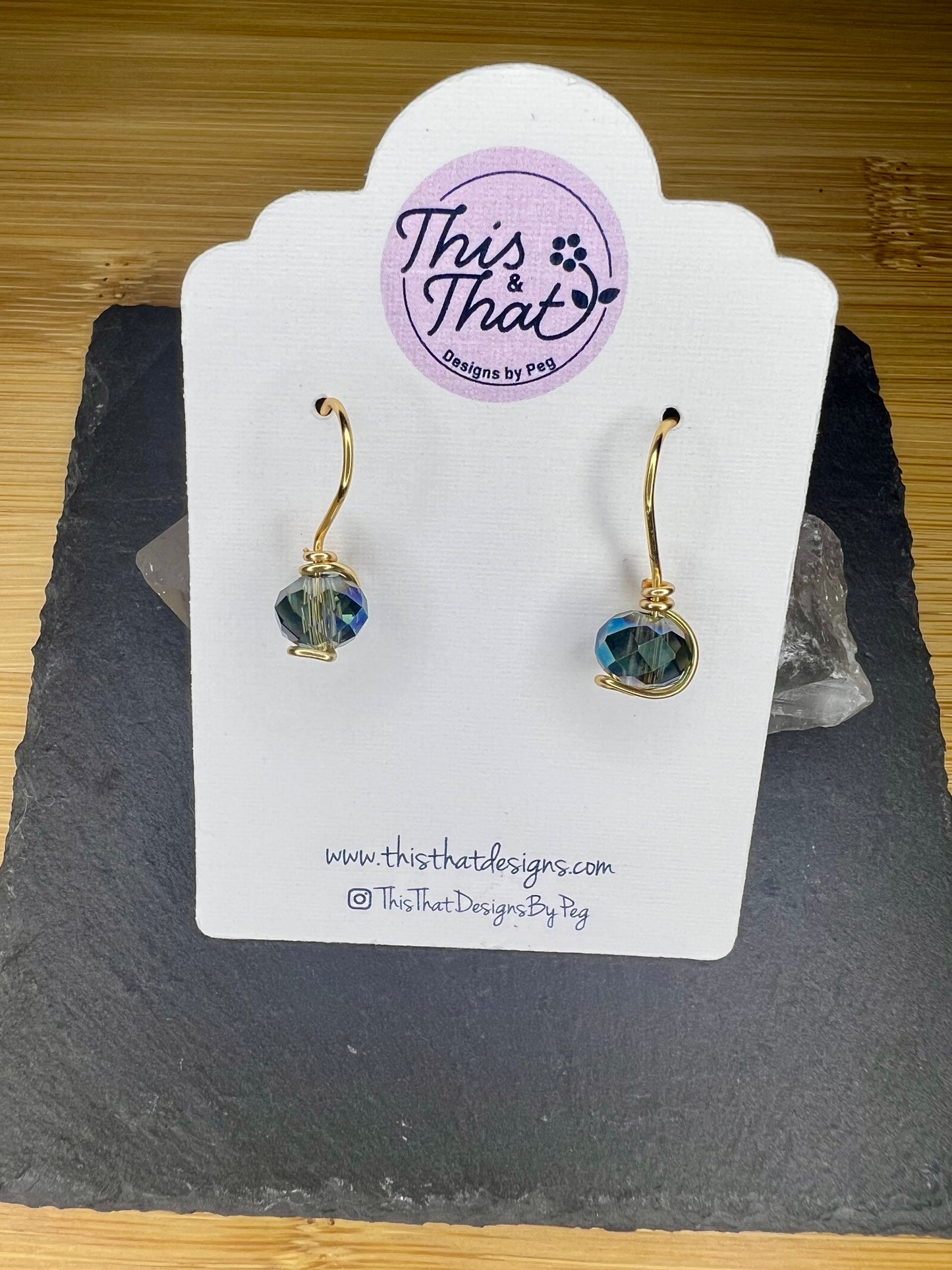 a pair of earrings displayed on a white card with a website address and a logo.