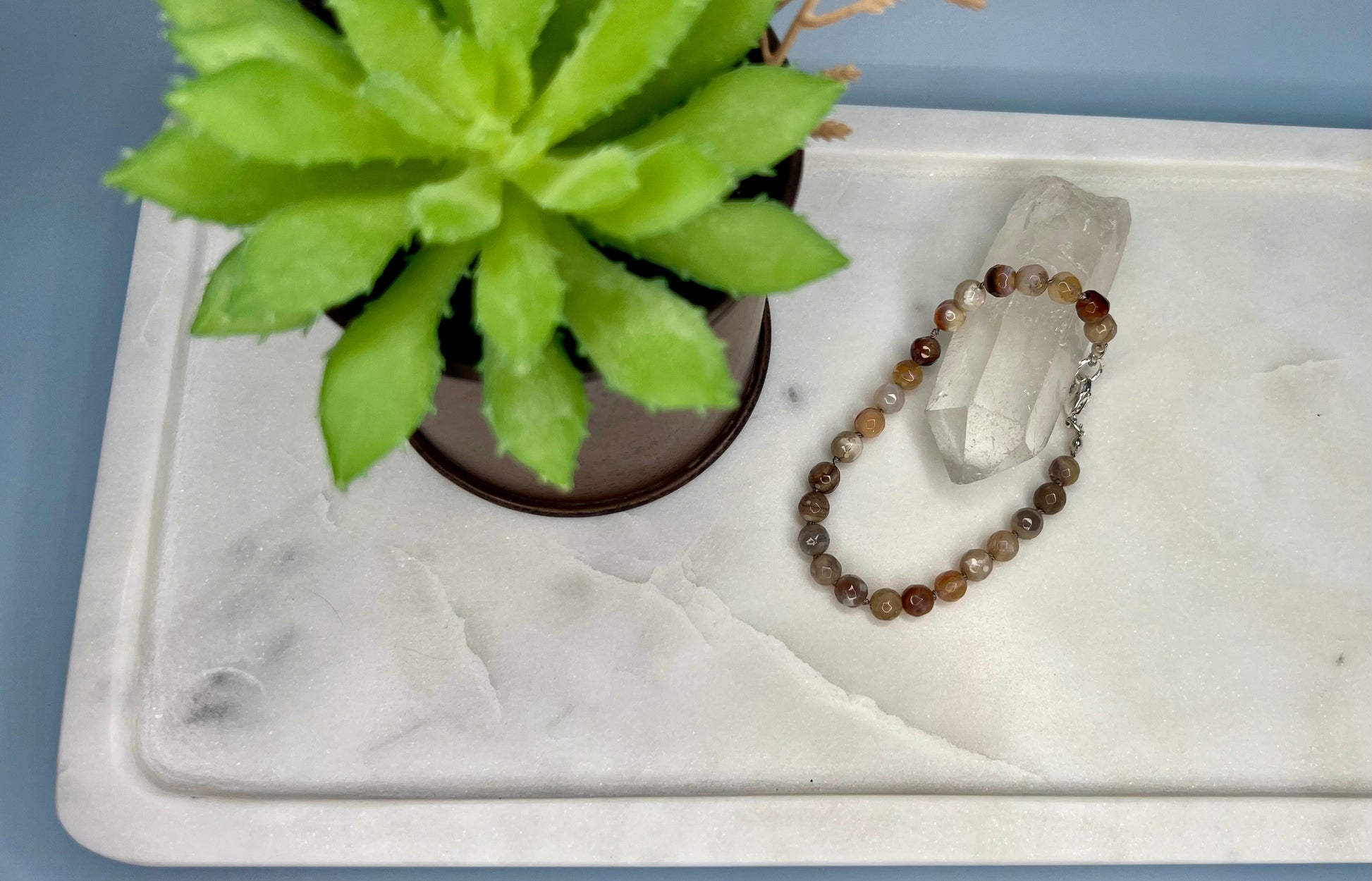 a white marble tray with a beaded bracelet and a green plant
