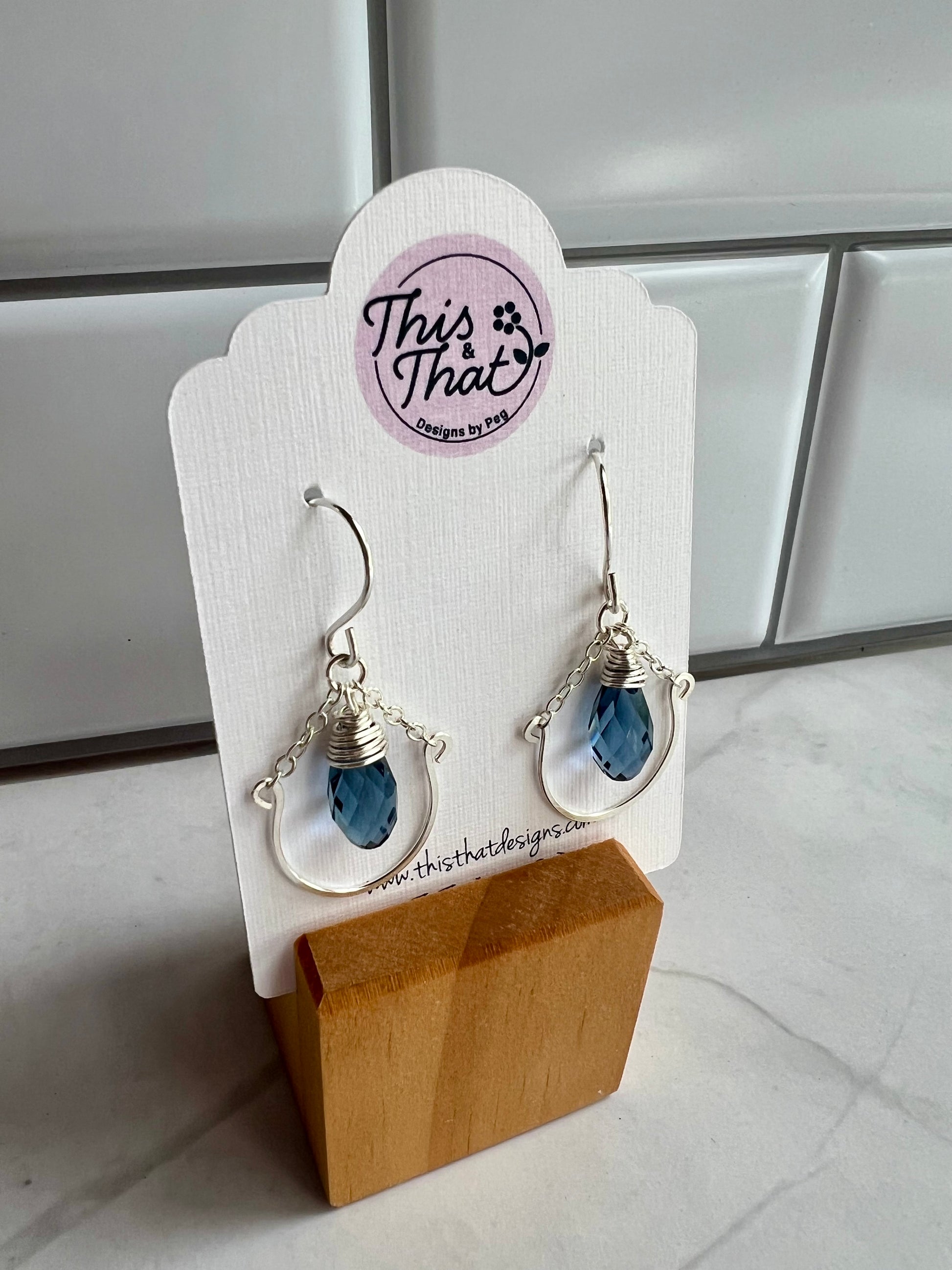 A pair of earrings with blue gemstones, displayed on a wooden stand.