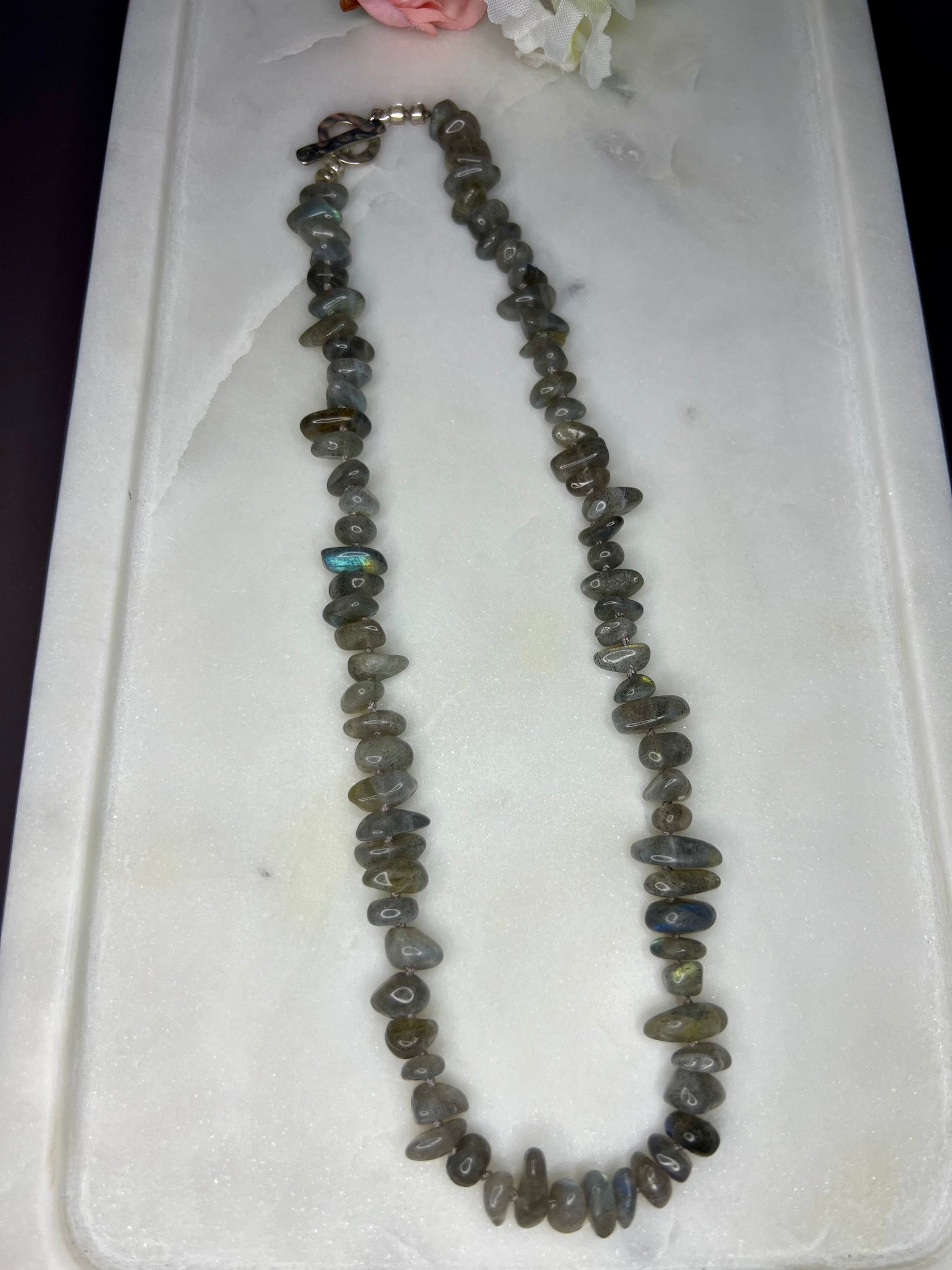 A necklace made of small, irregularly shaped stones in various shades of gray, brown, and black, resting on a white surface.