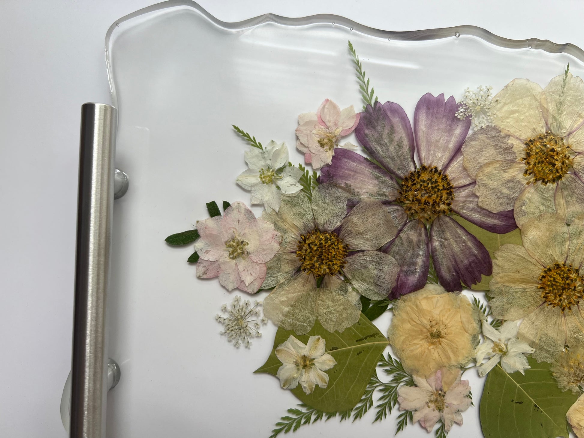 a close-up view of a glass tray with a floral arrangement of various flowers, including white, purple, and yellow flowers, along with green leaves.