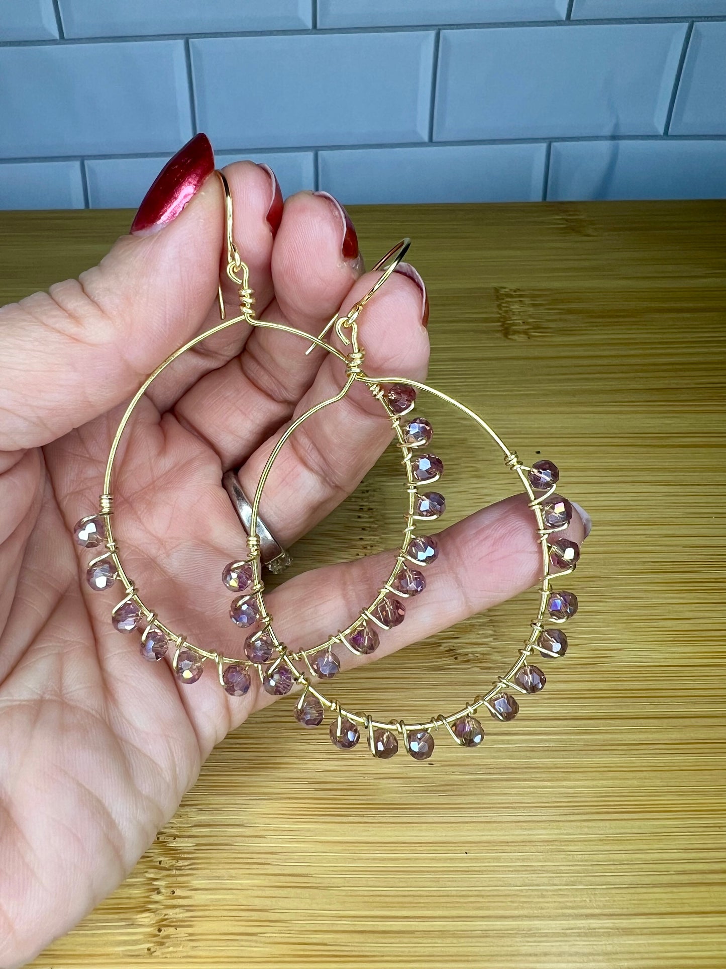 A hand holding a pair of gold hoop earrings with small purple gemstones hanging from them.