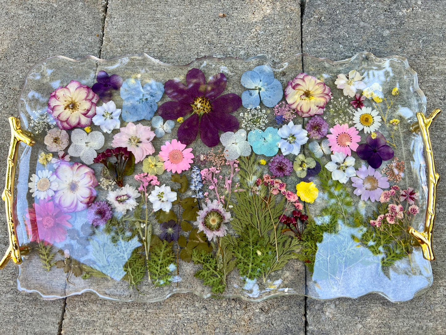 a clear glass tray with a gold handle, filled with a variety of colorful flowers and leaves.