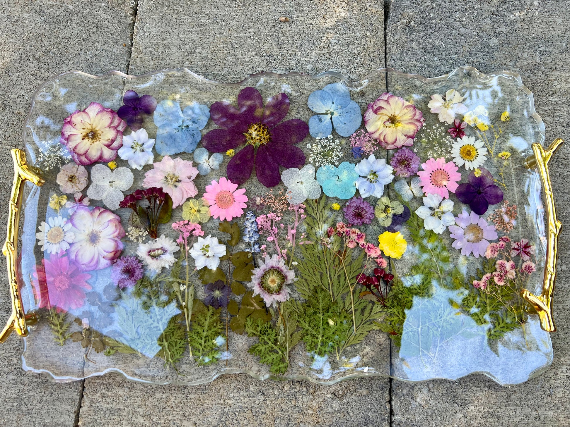 a clear glass tray with a gold handle, filled with a variety of colorful flowers and leaves.