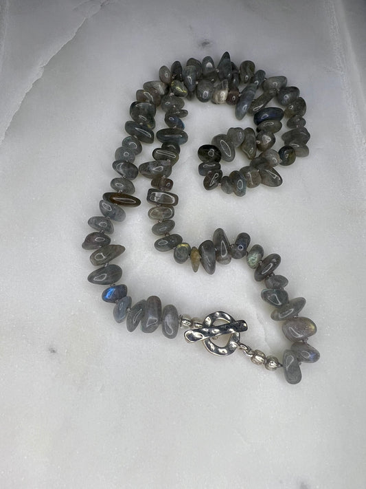 a necklace with gray beads and a silver clasp, resting on a white surface.