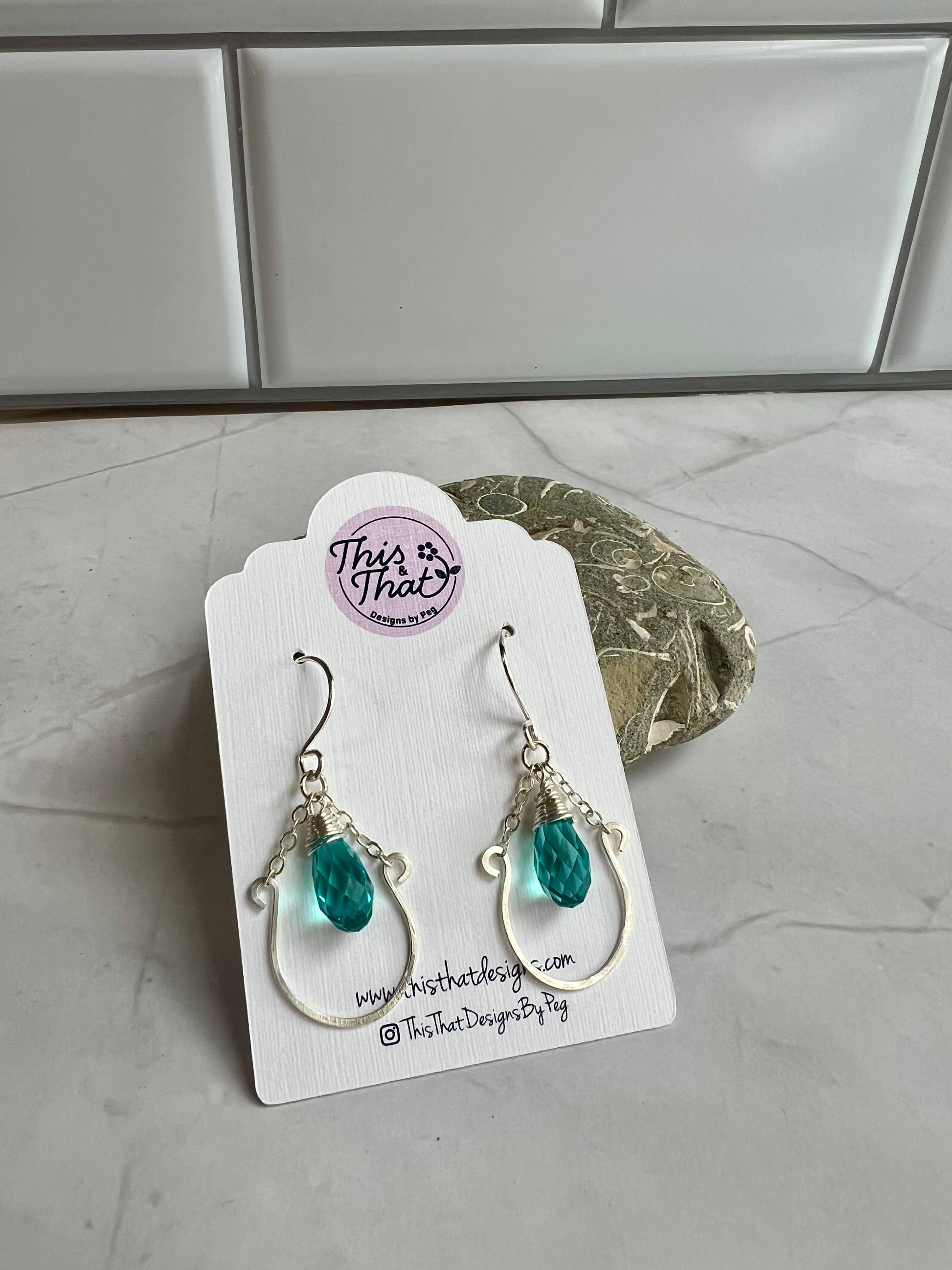 This image shows a pair of earrings with turquoise stones, displayed on a white card with a website address and a social media handle.