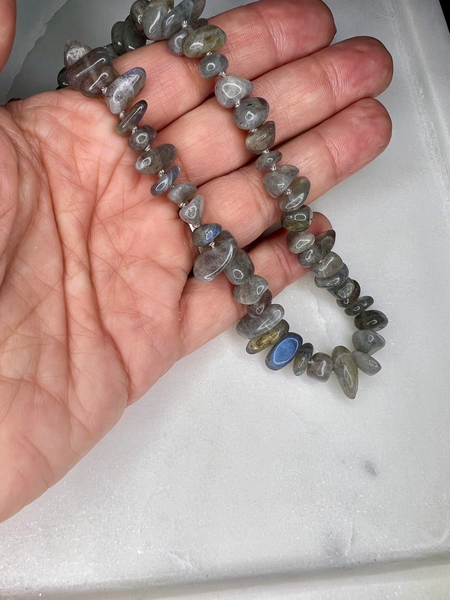 A hand holding a necklace made of gray and blue stones.