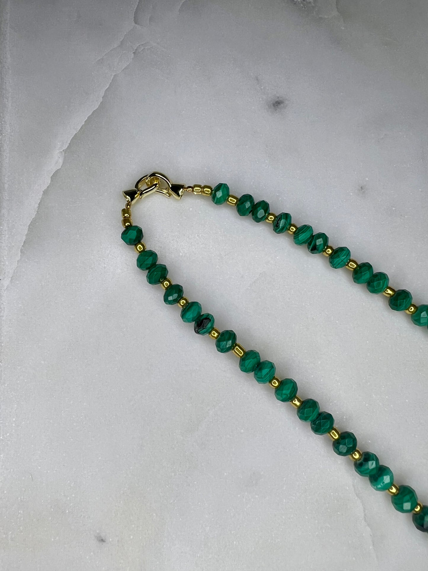 A necklace with green beads and a gold clasp is displayed on a white marble surface.