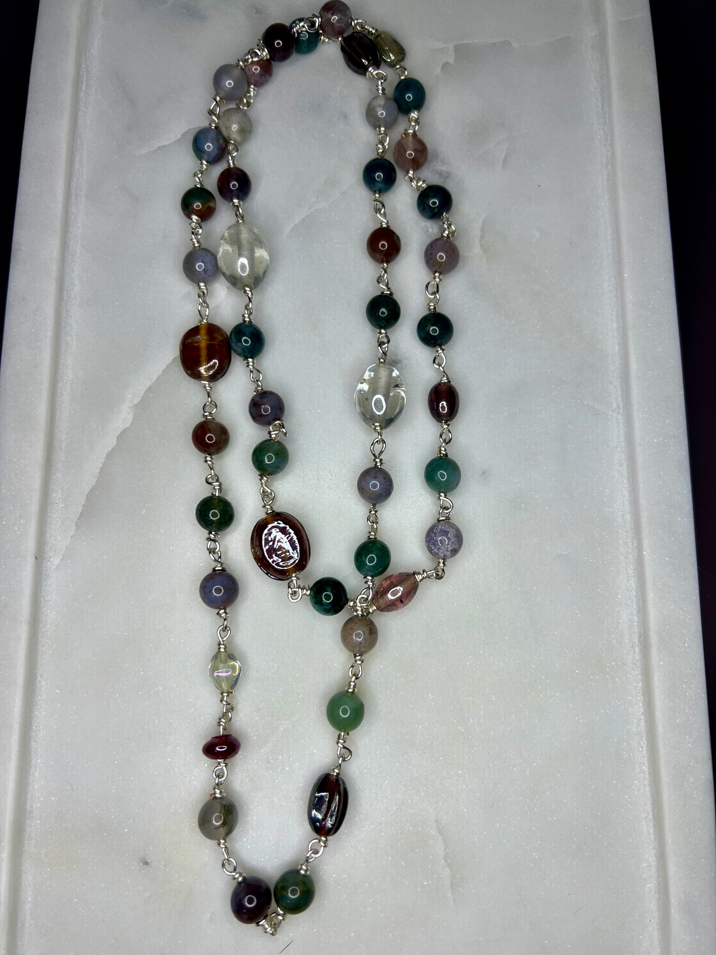 a necklace with various colored beads, including green, brown, and clear beads, arranged in a long chain.