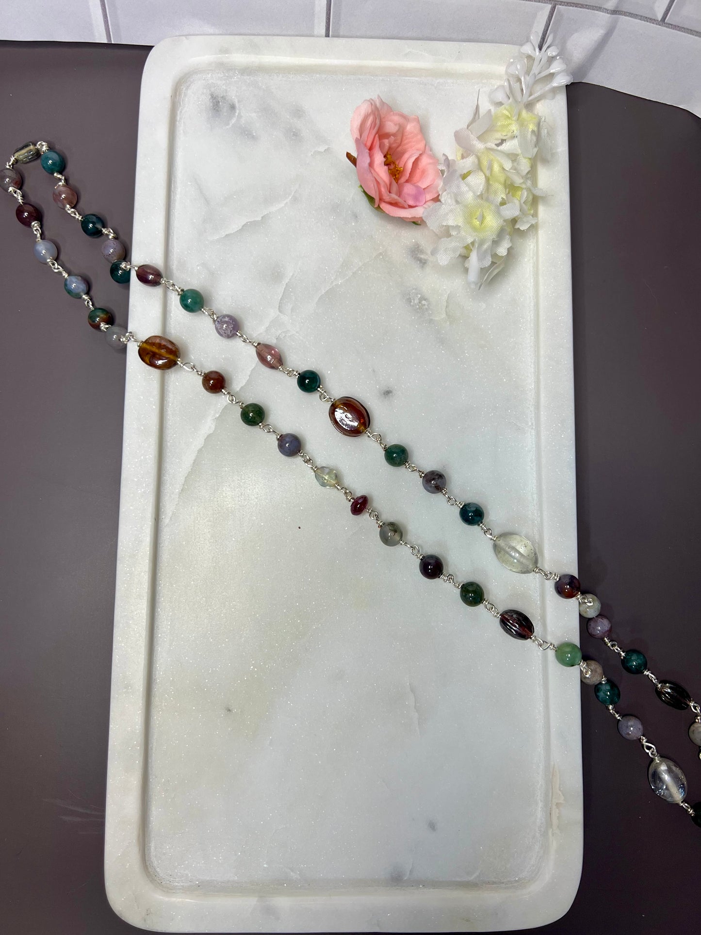 a necklace with colorful beads and a pink flower resting on a white marble tray.