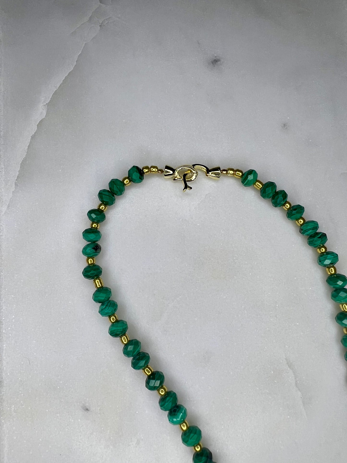 A necklace with green beads and gold accents, resting on a white marble surface.