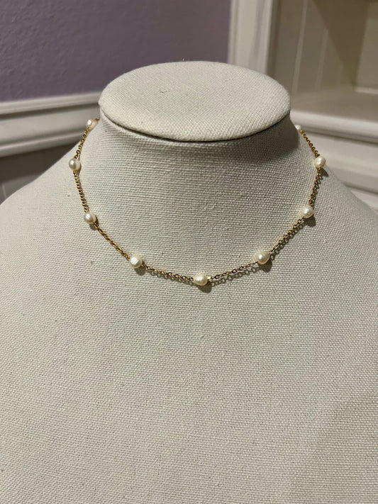 A necklace with a chain and small white pearls is displayed on a mannequin.