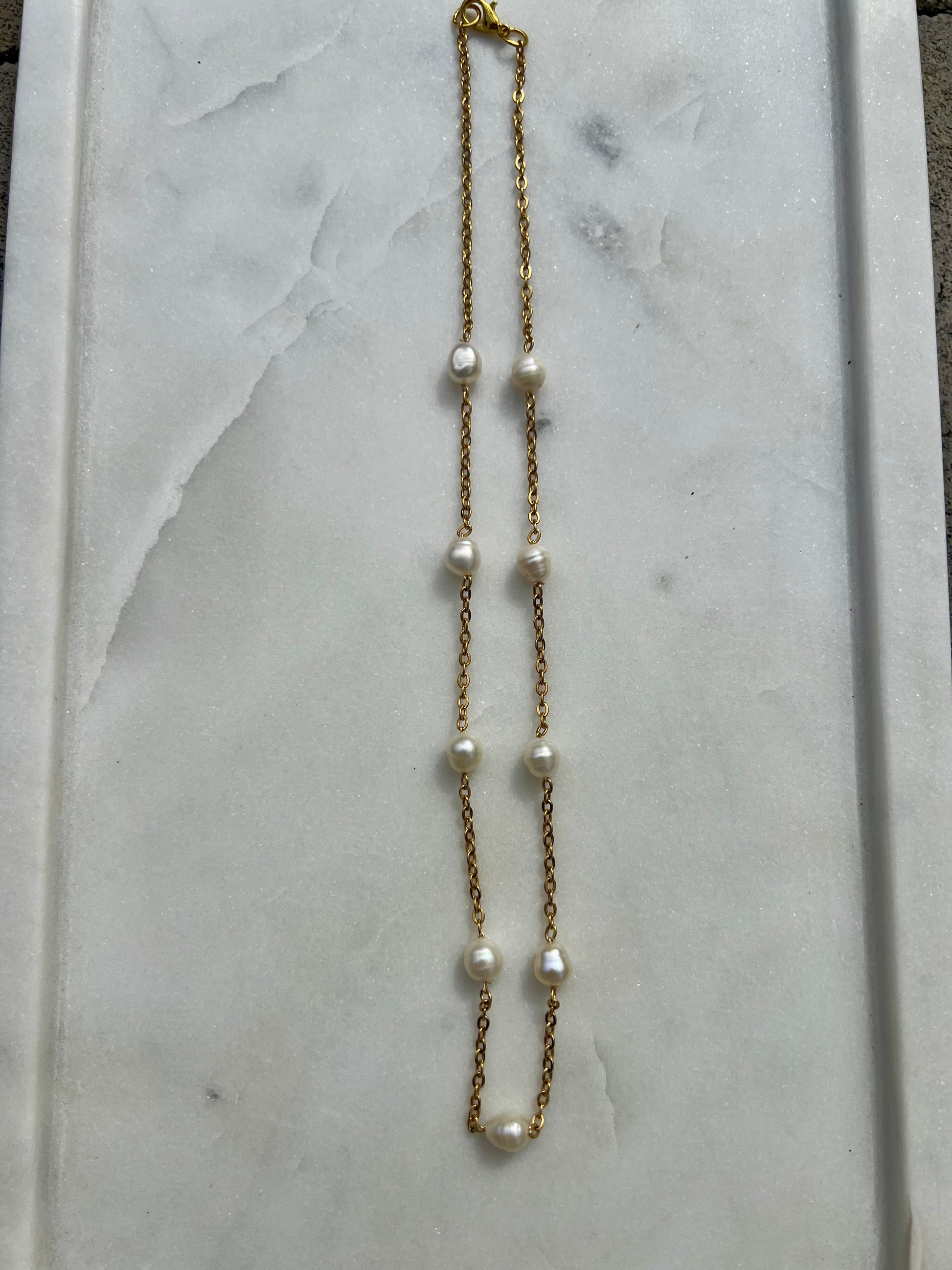 A necklace with a gold chain and white pearls is displayed on a white marble surface.