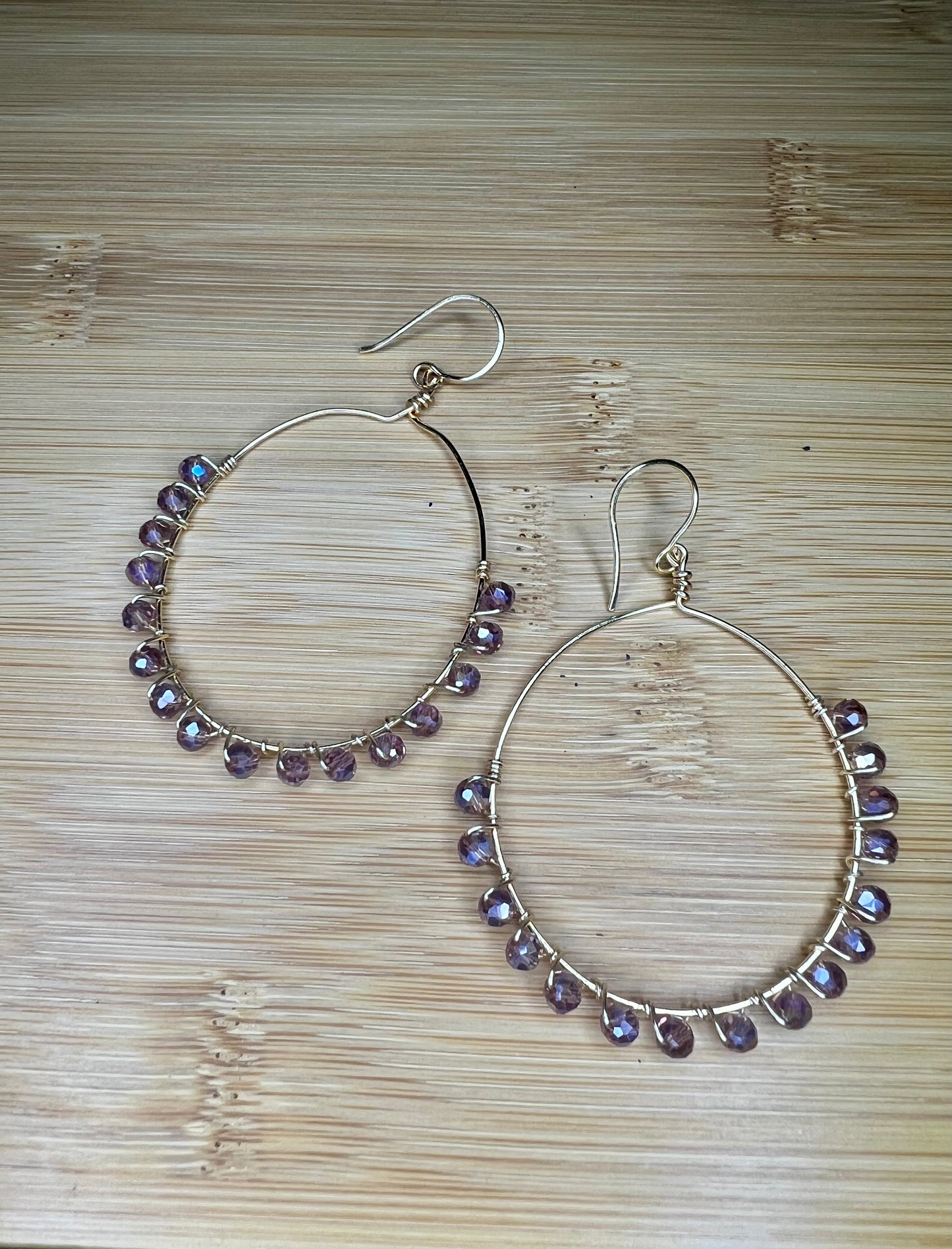 A pair of silver hoop earrings with purple gemstone beads hanging from them, placed on a wooden surface.