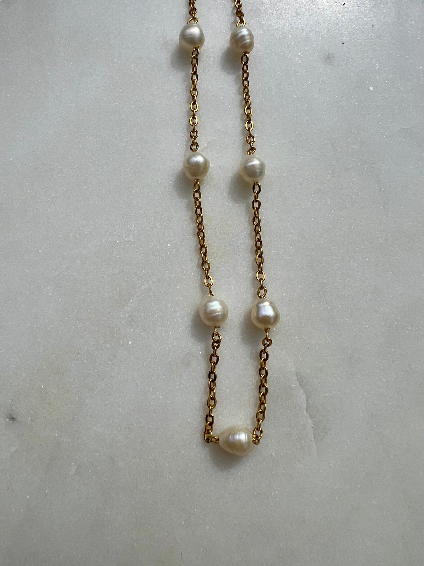 A necklace with a series of white pearls and a gold chain is displayed against a white marble background.