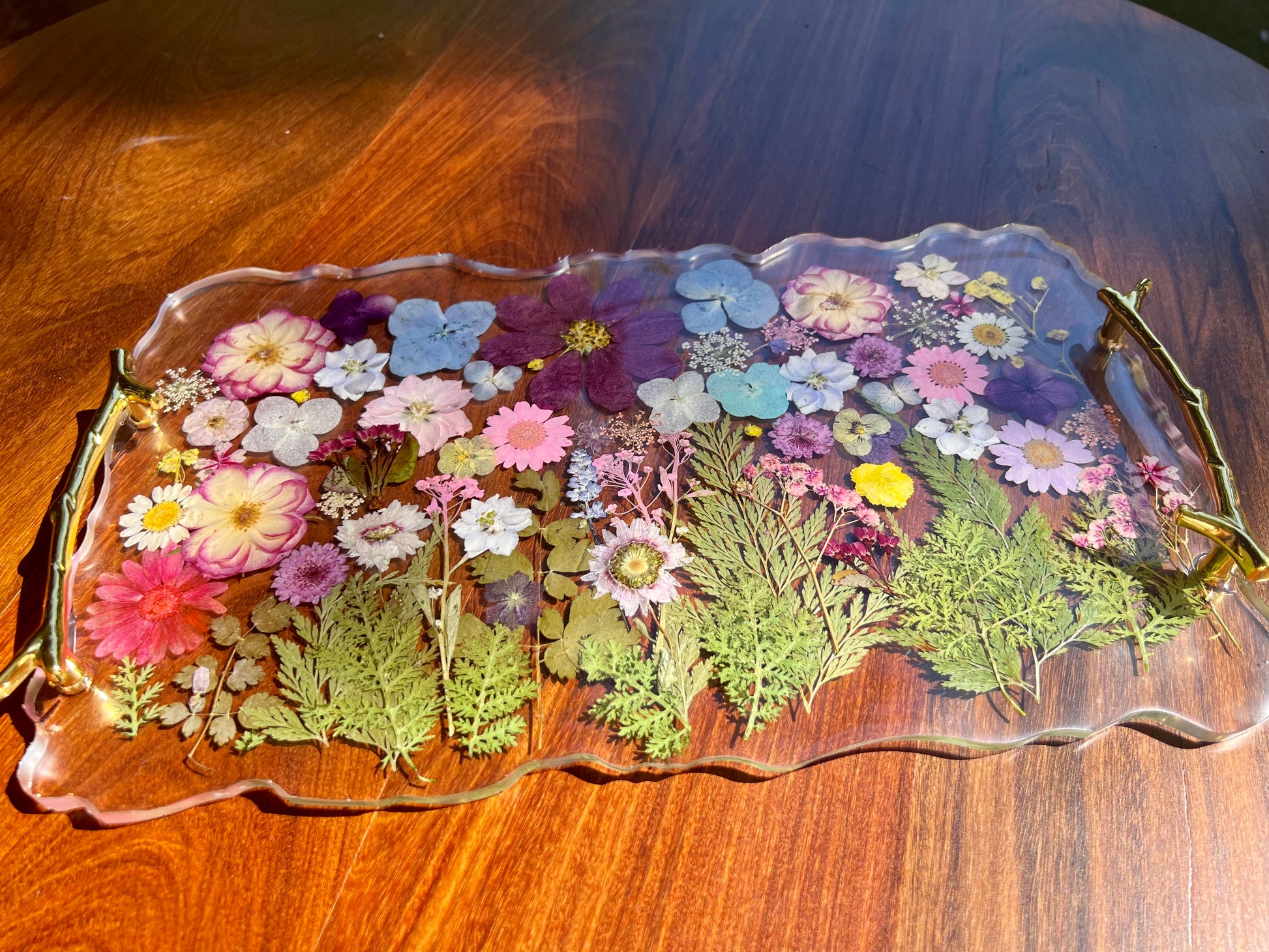 A clear glass tray with a floral arrangement of various colorful flowers and leaves displayed on it.