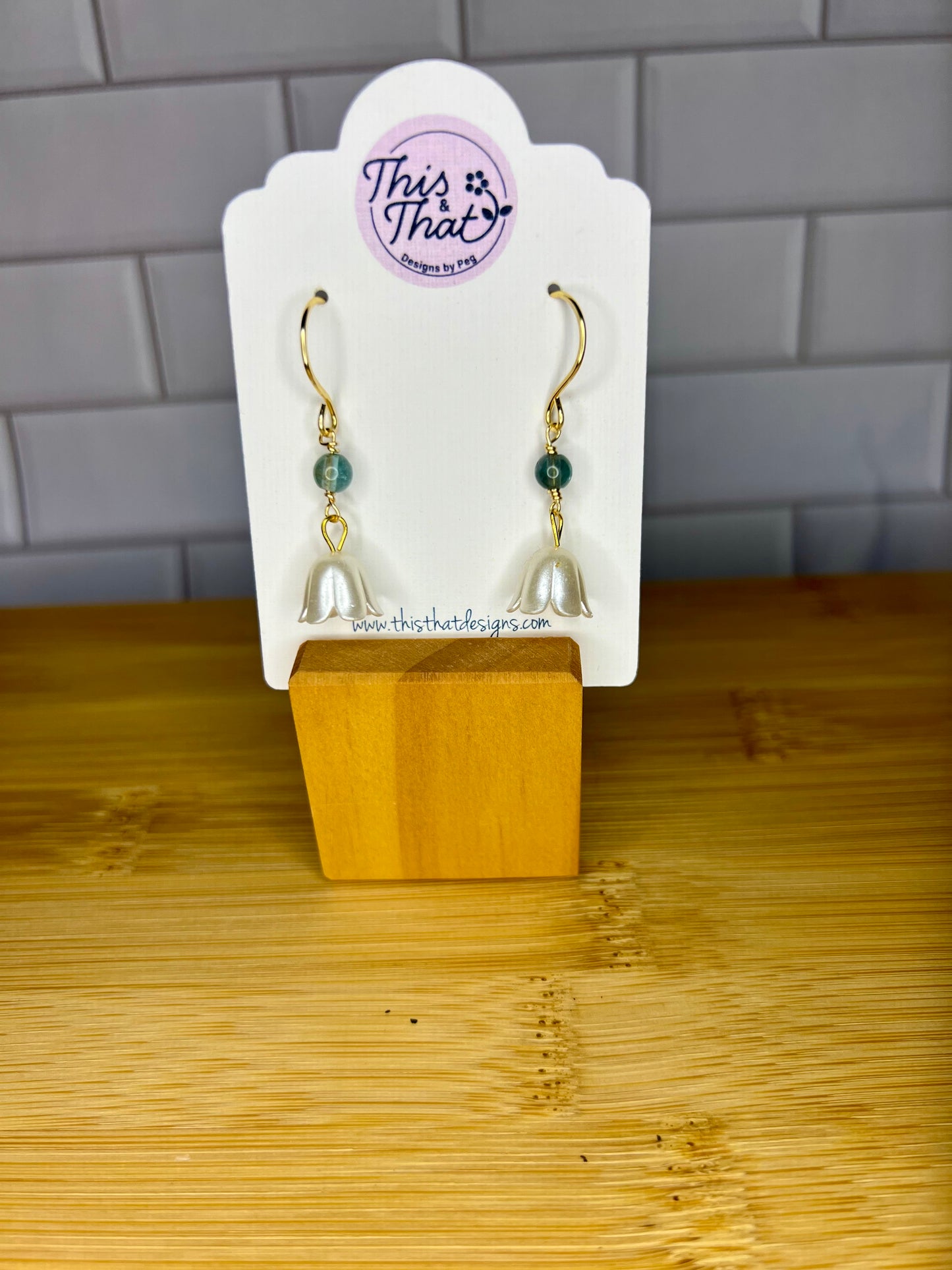 A pair of earrings with white shells and green stones, displayed on a wooden stand.