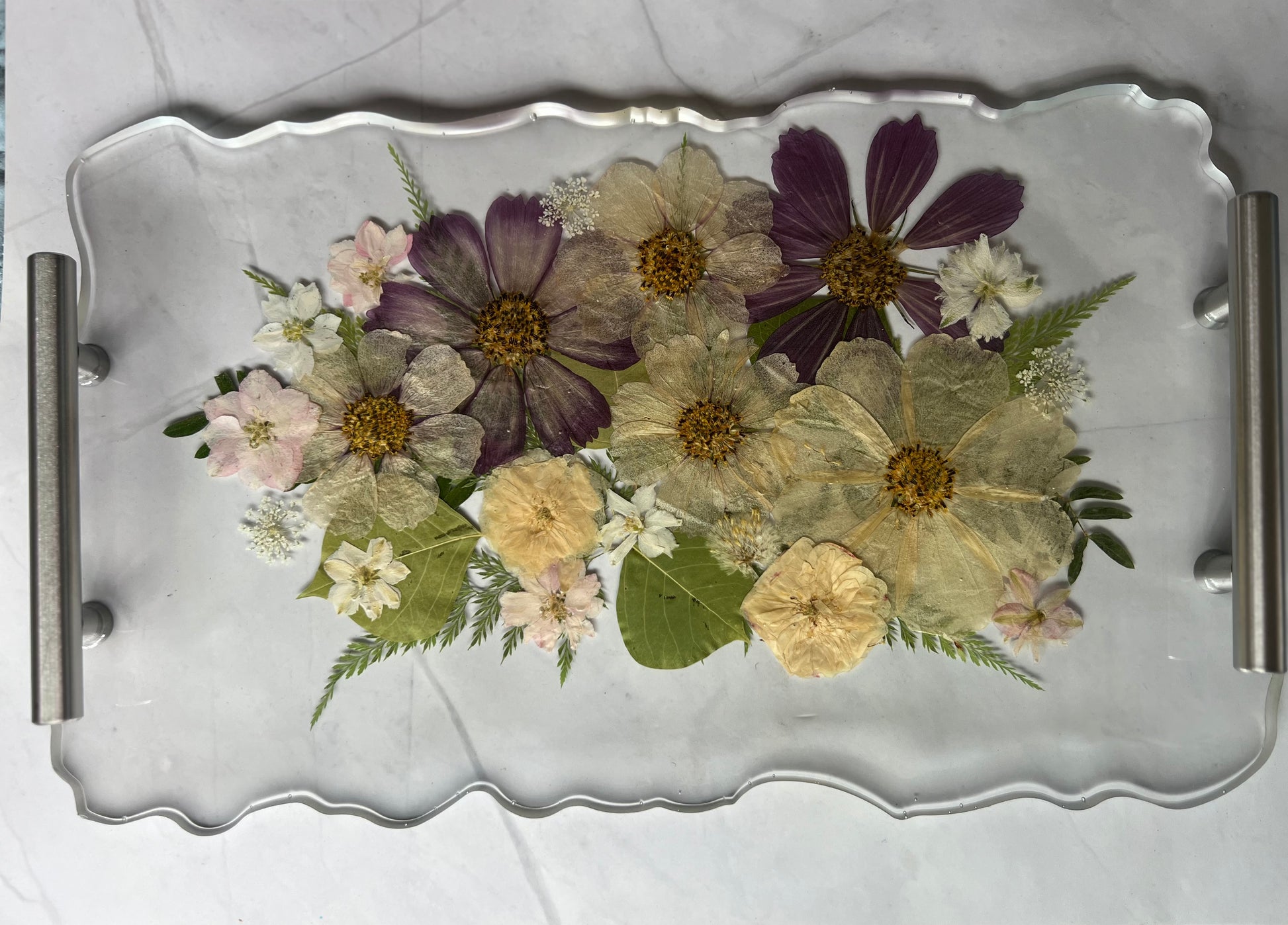 A clear glass tray with a variety of colorful flowers and leaves arranged on it.