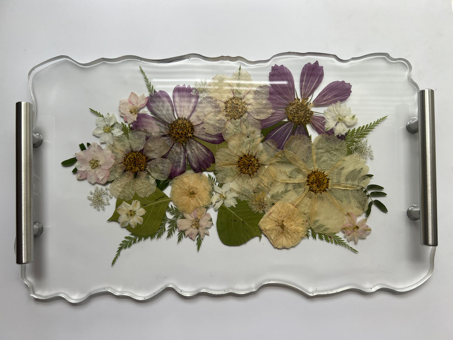 a clear glass tray with a floral arrangement of various flowers, including purple and white flowers, as well as some green leaves.