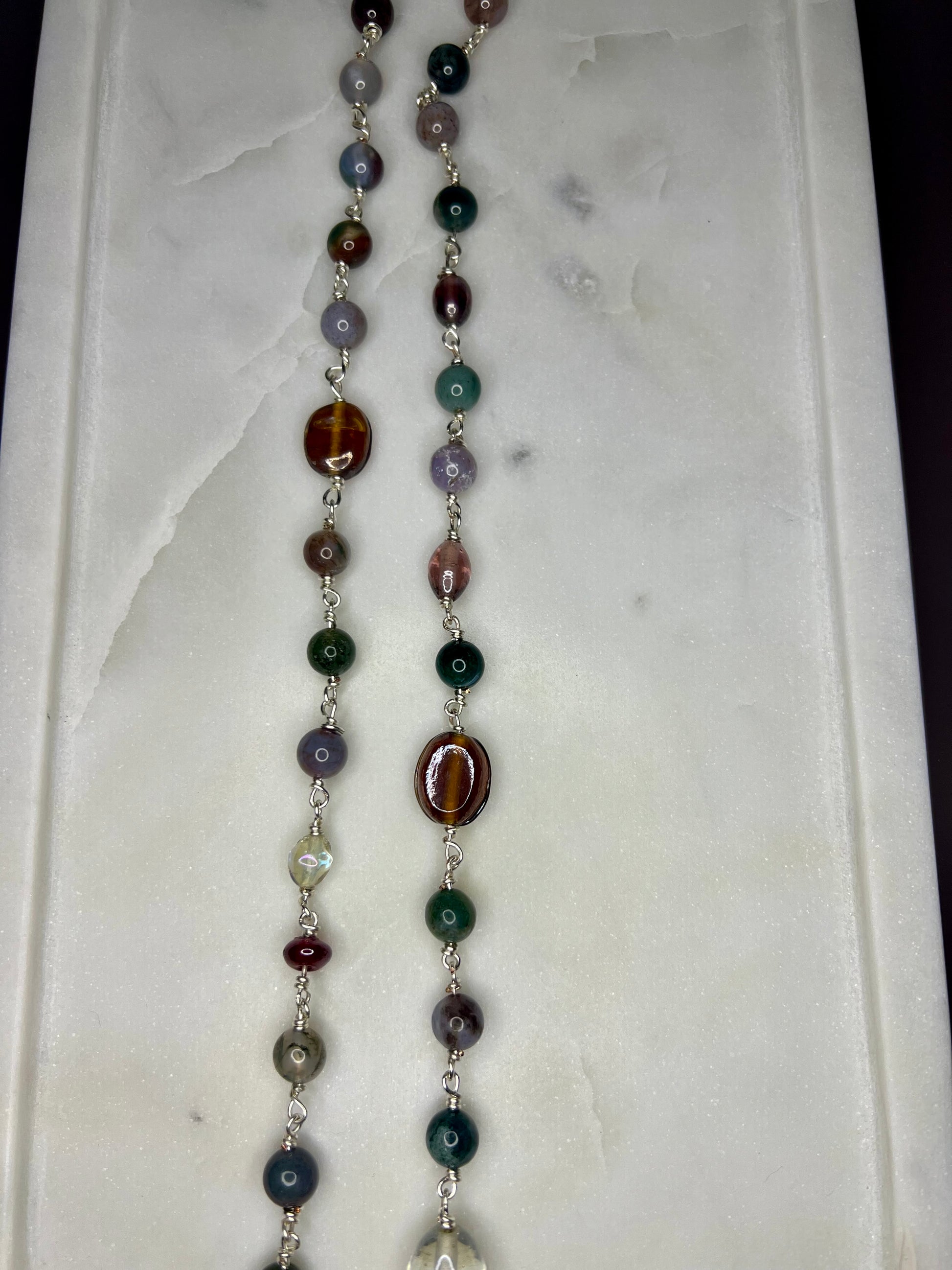 a necklace with a variety of colorful beads, including green, purple, and brown beads, arranged in a row on a white surface.