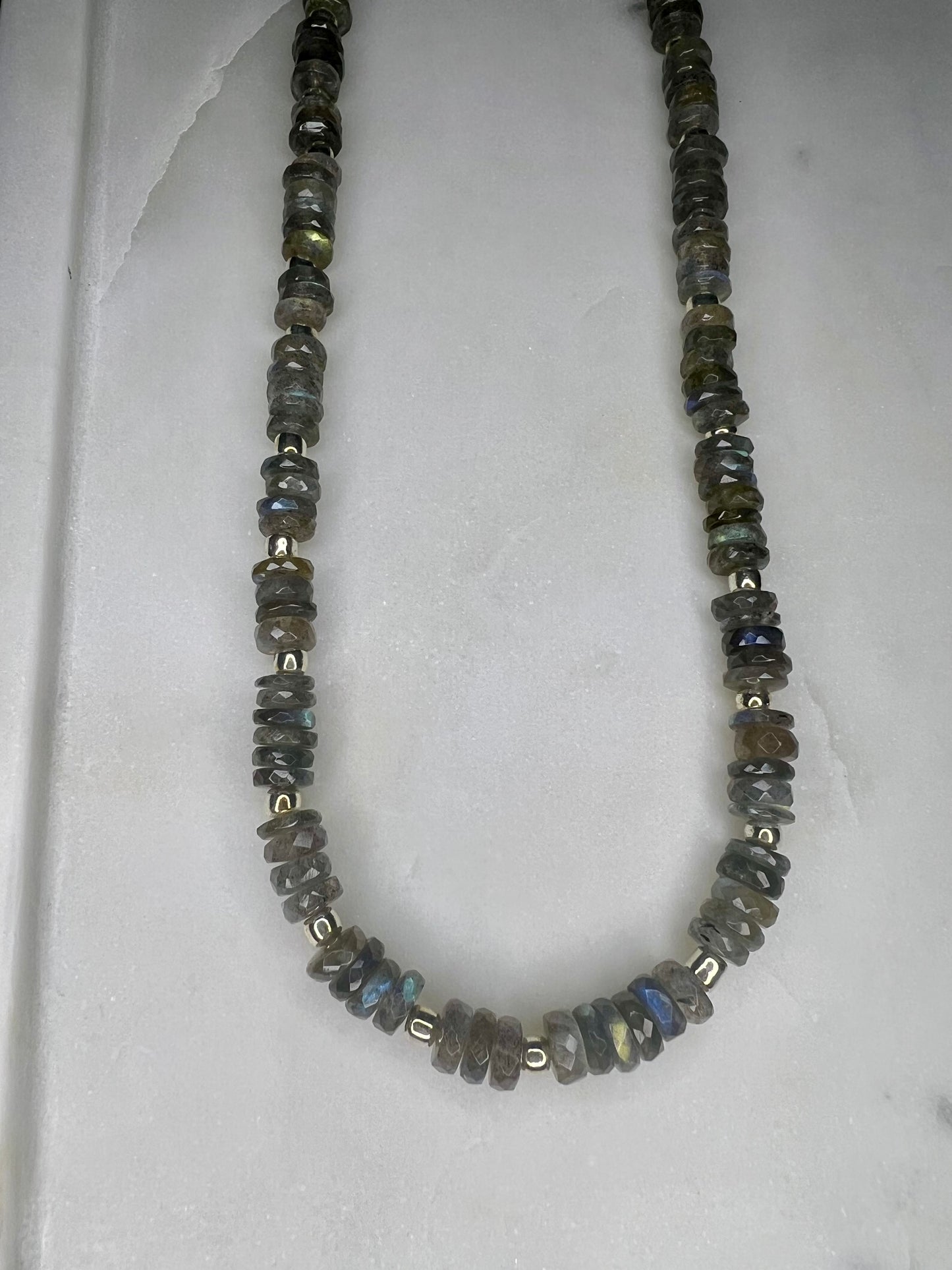 A necklace made of small, round, multicolored stones or beads, arranged in a row and secured with metal clasps.