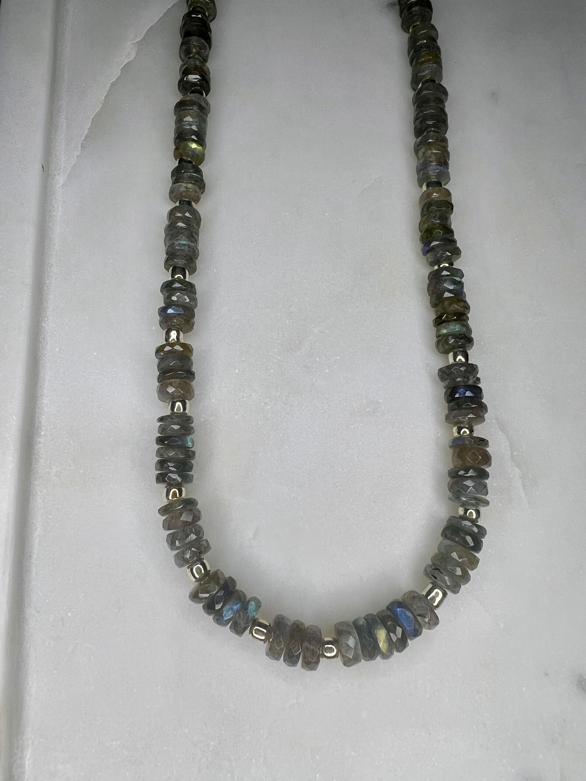 A necklace made of small, round, multicolored stones or beads, arranged in a row and secured with metal clasps.