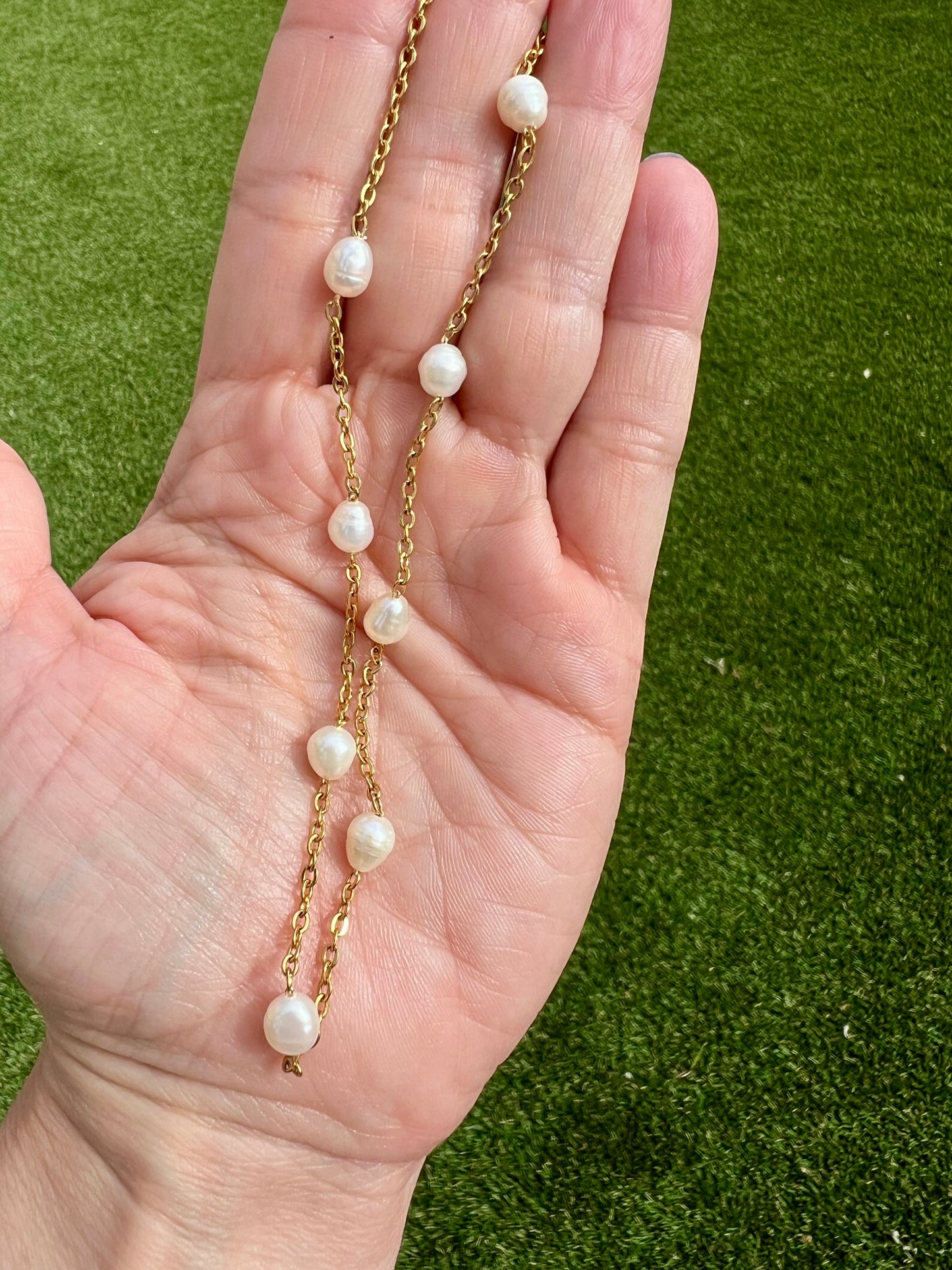 A hand holding a delicate gold necklace with white pearls.