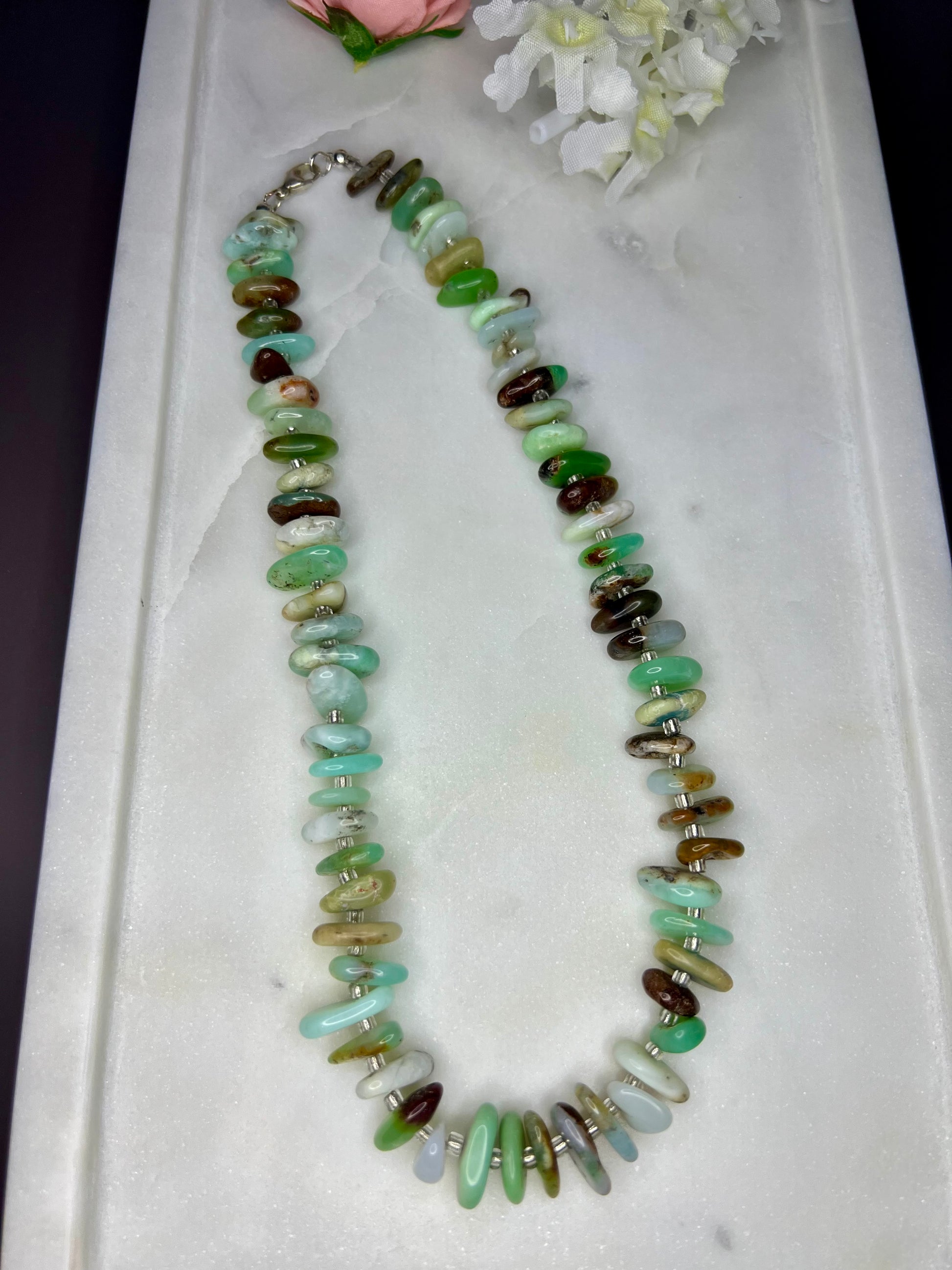 A necklace made of various colored stones, including green, brown, and white, is displayed on a white surface.