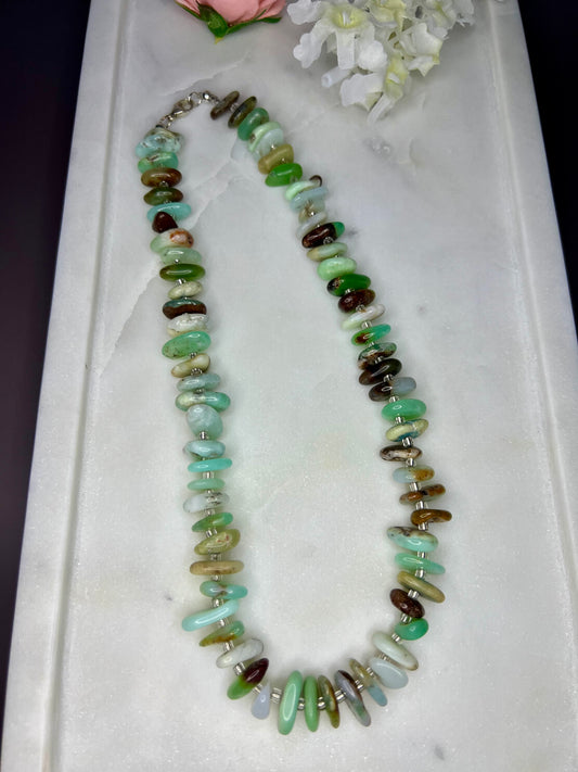 A necklace made of various colored stones, including green, brown, and white, is displayed on a white surface.