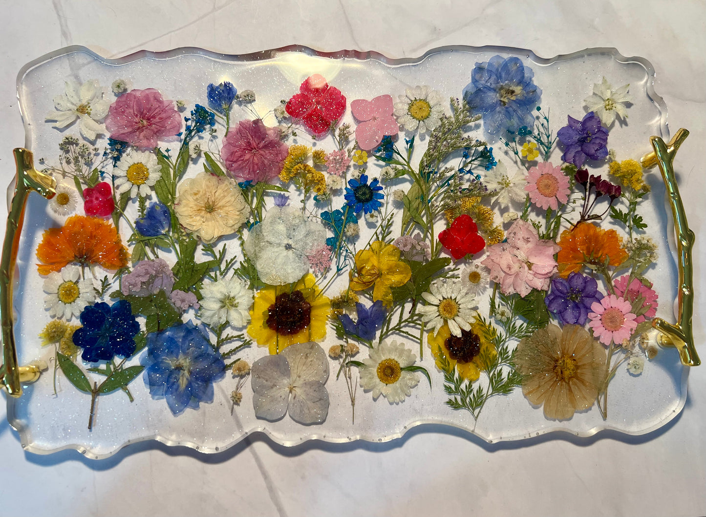 a clear glass tray with a variety of colorful flowers, including sunflowers, daisies, and other blooms, arranged on it.