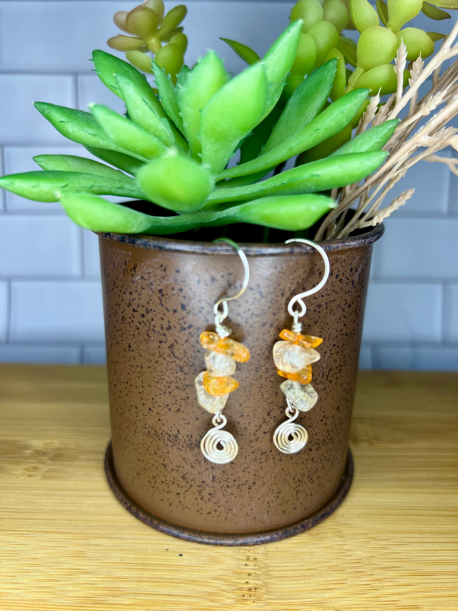 A pair of earrings with orange and white stones hanging from them, placed in a brown ceramic container or vase.