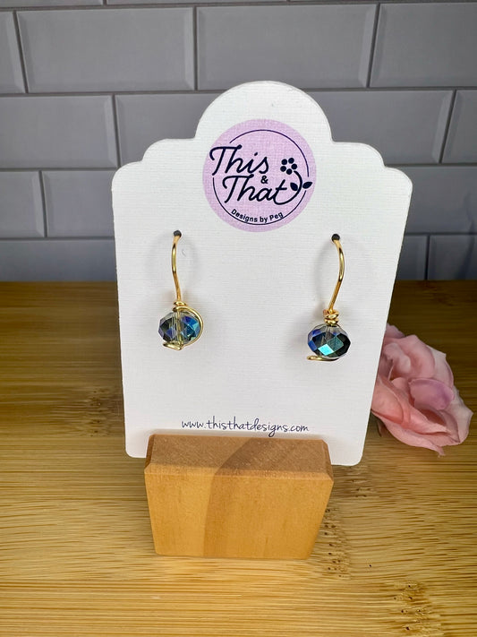 a pair of earrings displayed on a white stand, with a pink flower in the background.