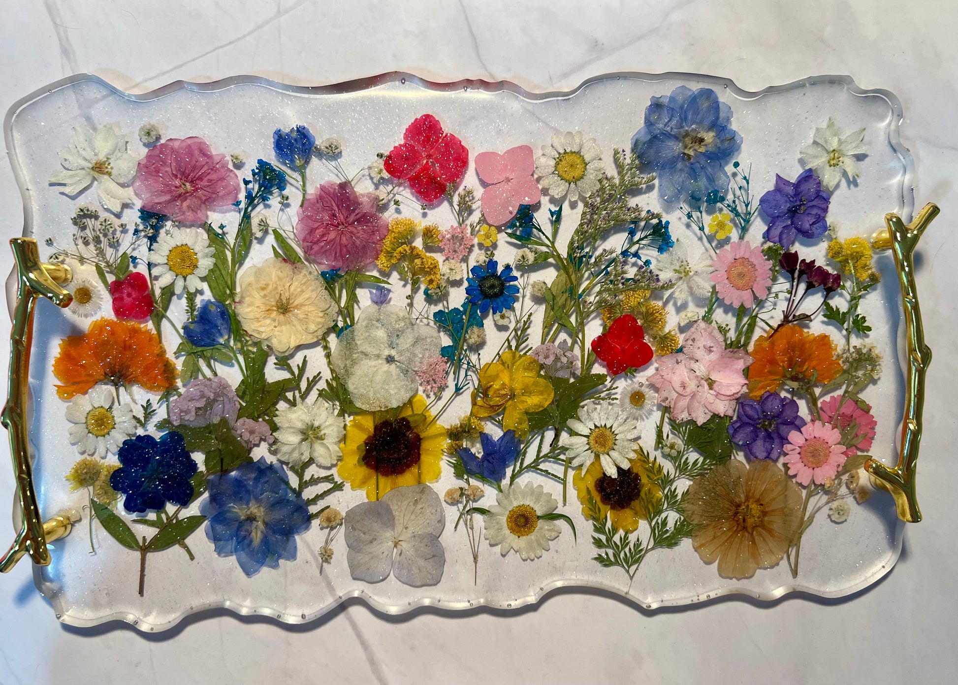 a clear tray with a variety of colorful flowers, including pink, blue, orange, and white flowers, as well as green leaves.