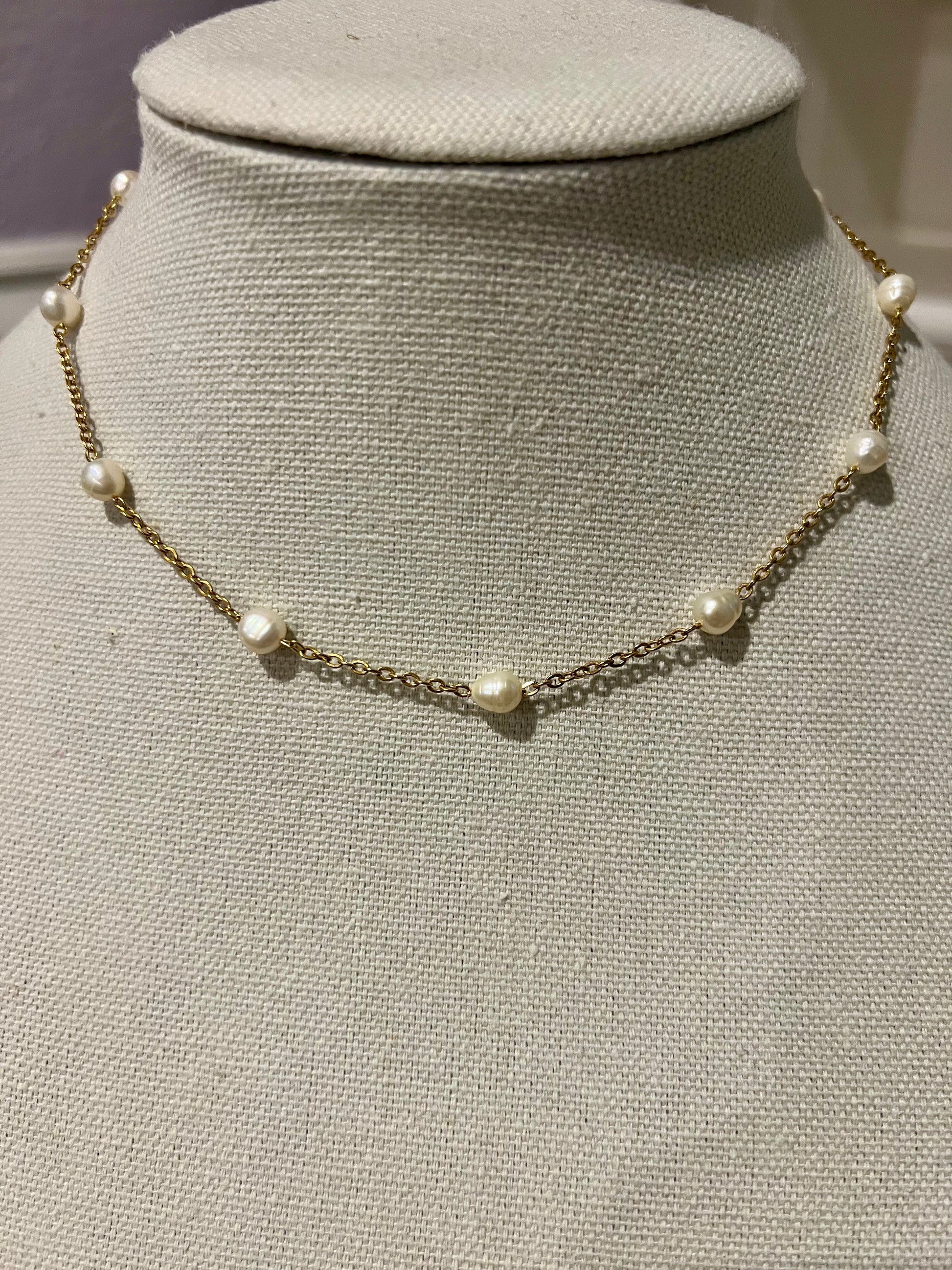 A necklace with a chain and small pearls on it, displayed on a mannequin.
