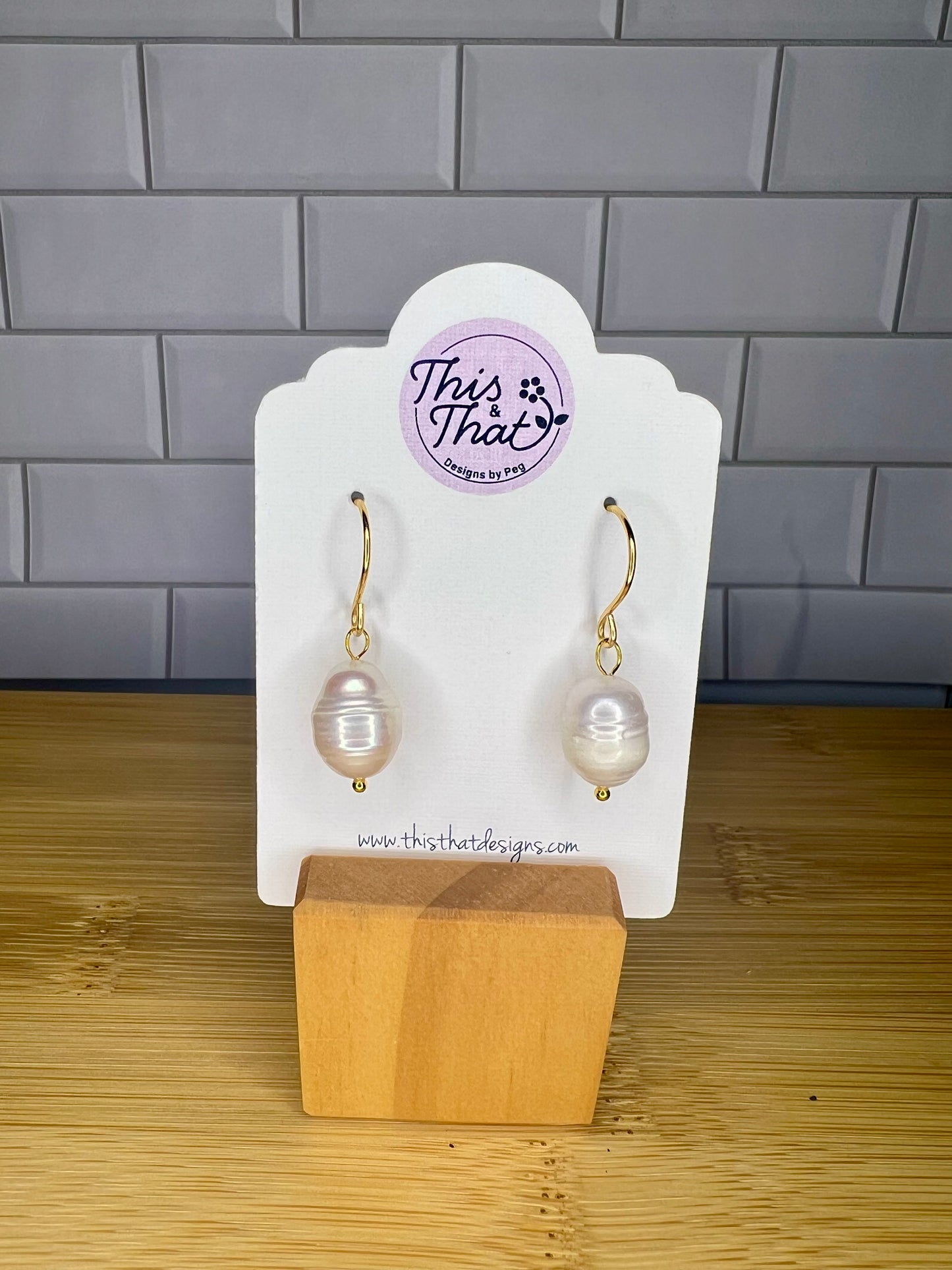 A pair of pearl earrings displayed on a white card stand, with a website address provided.