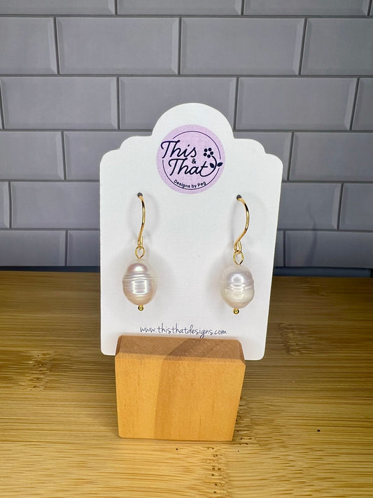 A pair of pearl earrings displayed on a white card stand, with a website address provided.