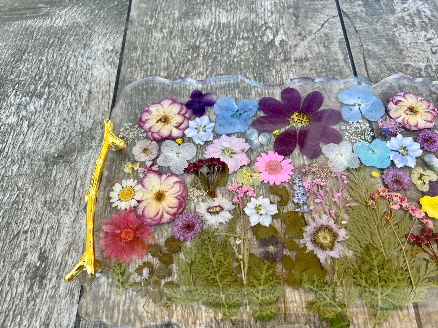 a clear tray with a variety of colorful flowers, including purple, pink, white, and yellow flowers, arranged on a wooden surface.