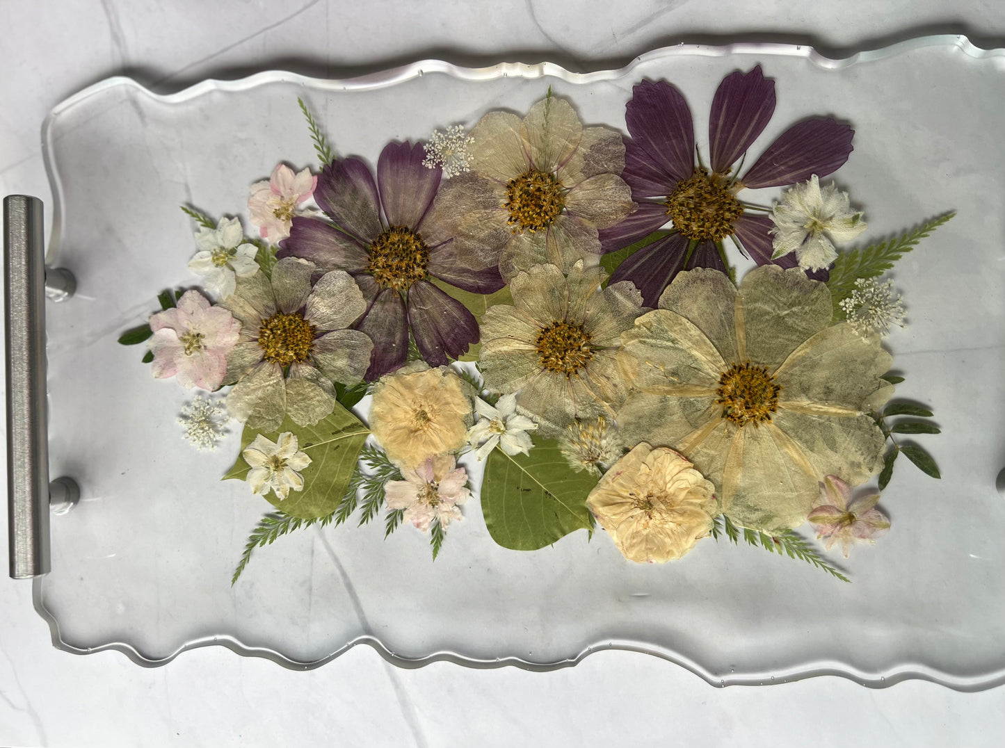A clear glass tray displaying a vibrant arrangement of dried flowers and leaves.
